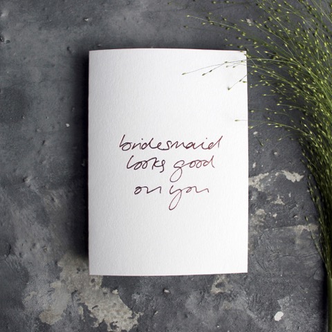 A white bridesmaid card against a grey backdrop that reads, bridesmaid looks good on you
