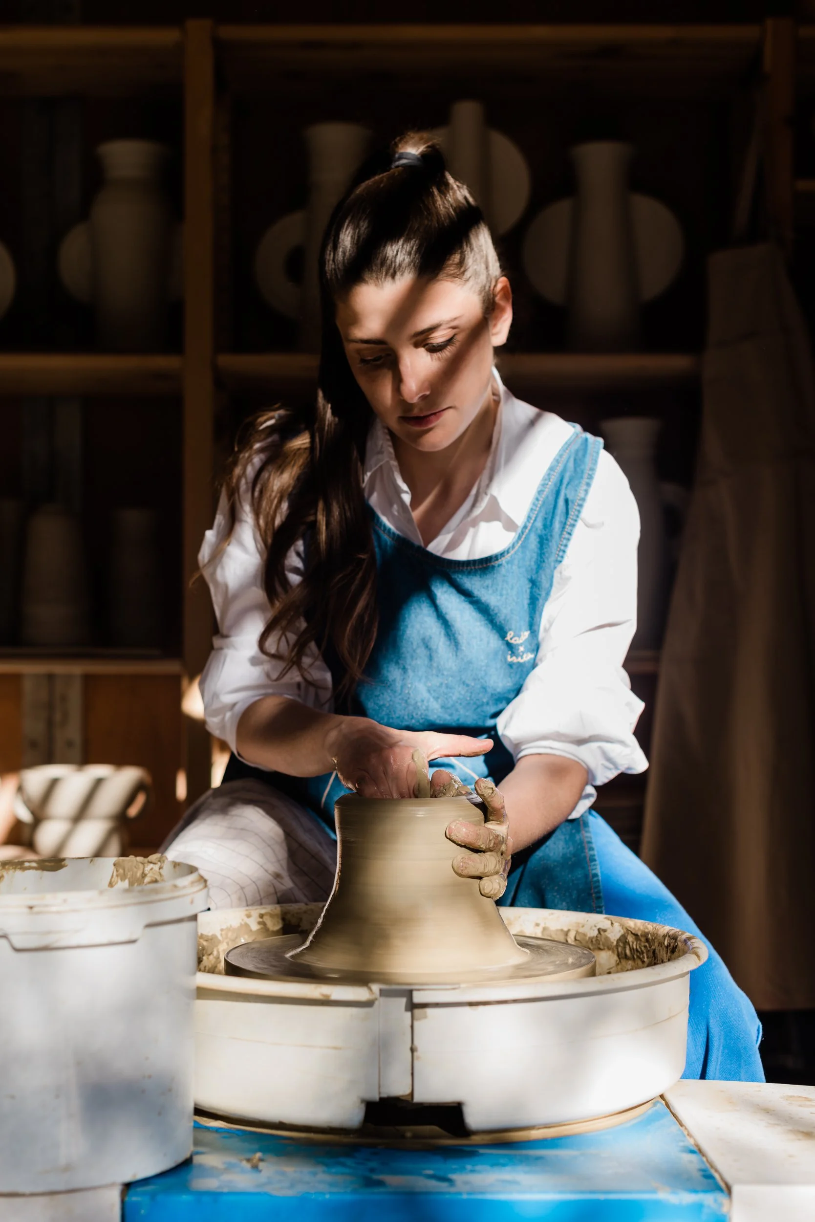 Woman shaping a ceramic pot on a pottery wheel in a workshop.
