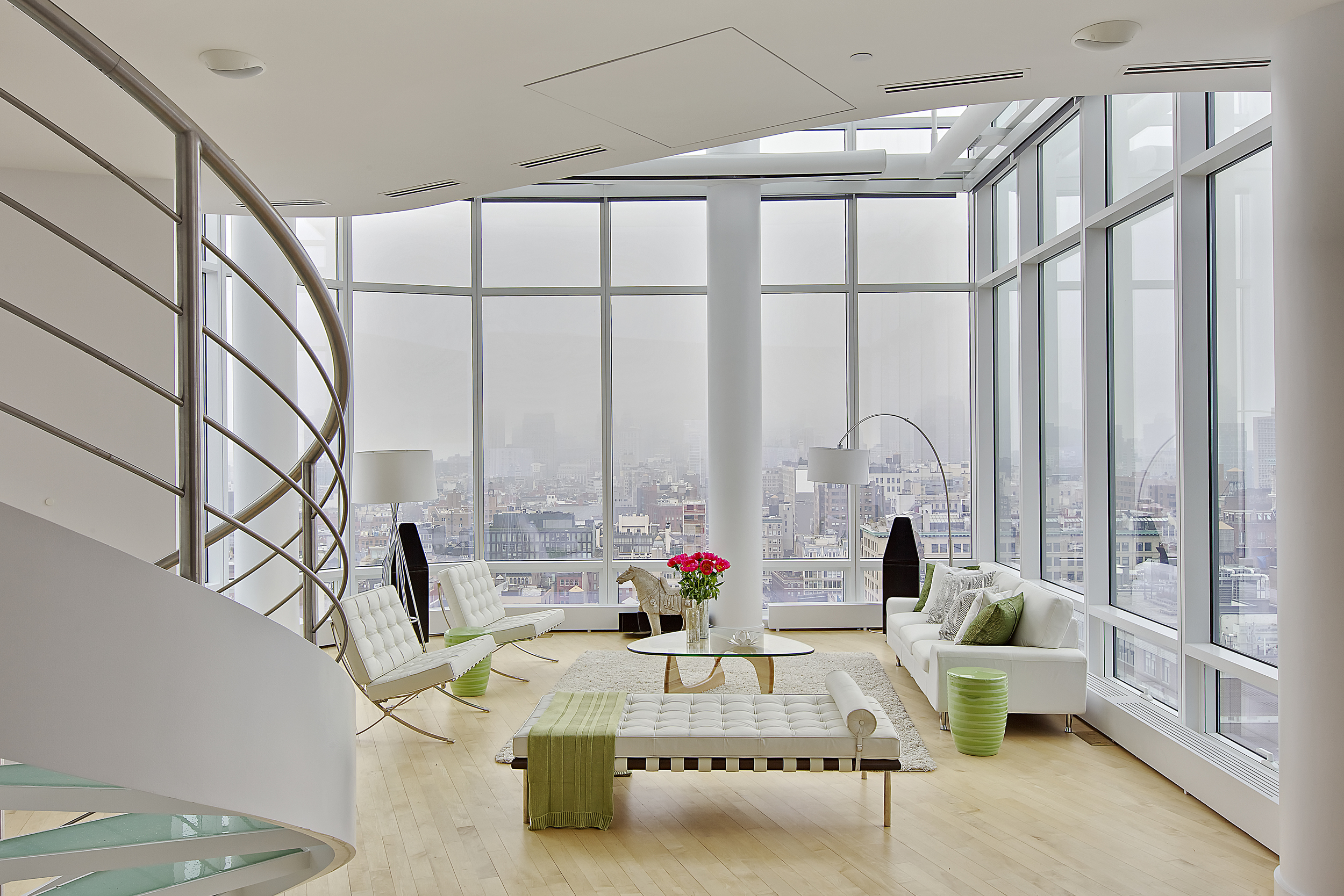   CHELSEA PENTHOUSE DUPLEX   The modern style provides an alluring view of the living room when combined with elegant furnishings. The glass walls and light flooring showcase a perfect combo. A glass coffee table with fresh red flowers complements th