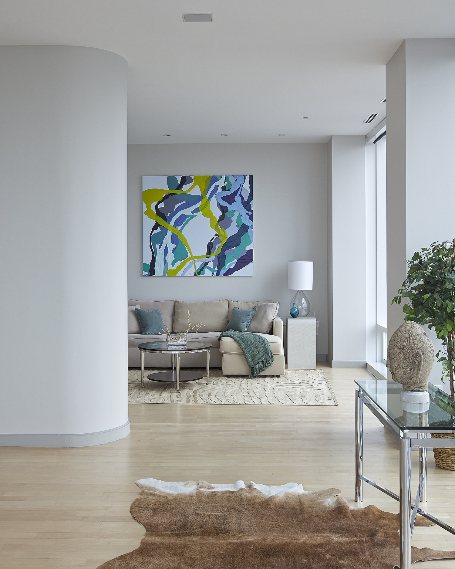  CHELSEA PENTHOUSE DUPLEX   A peaceful foyer with a Buddha sculpture on a glass table gives a glimpse of a cozy living room. The animal skin rug and a plant give natural vibes as you walk through the foyer. A glass wall allows a considerable amount o