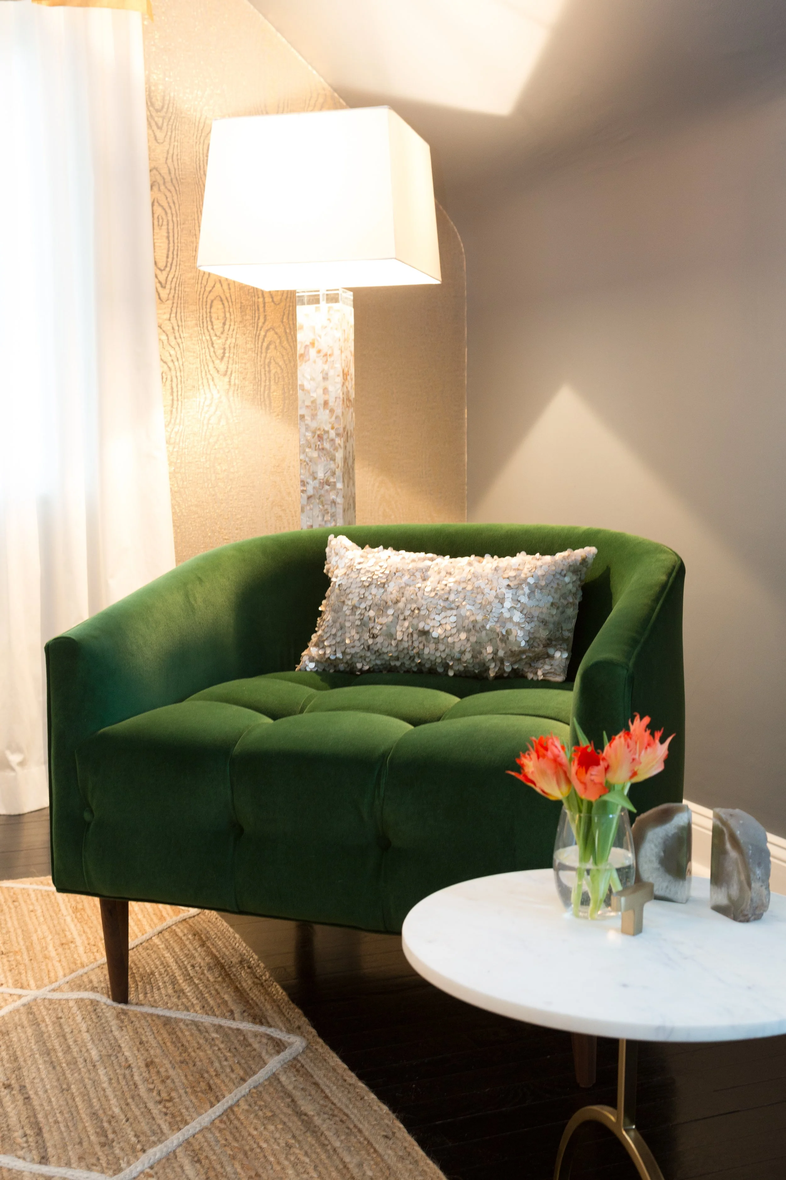 Tufted emerald velvet armchair beside a marble side table and warm floor lamp