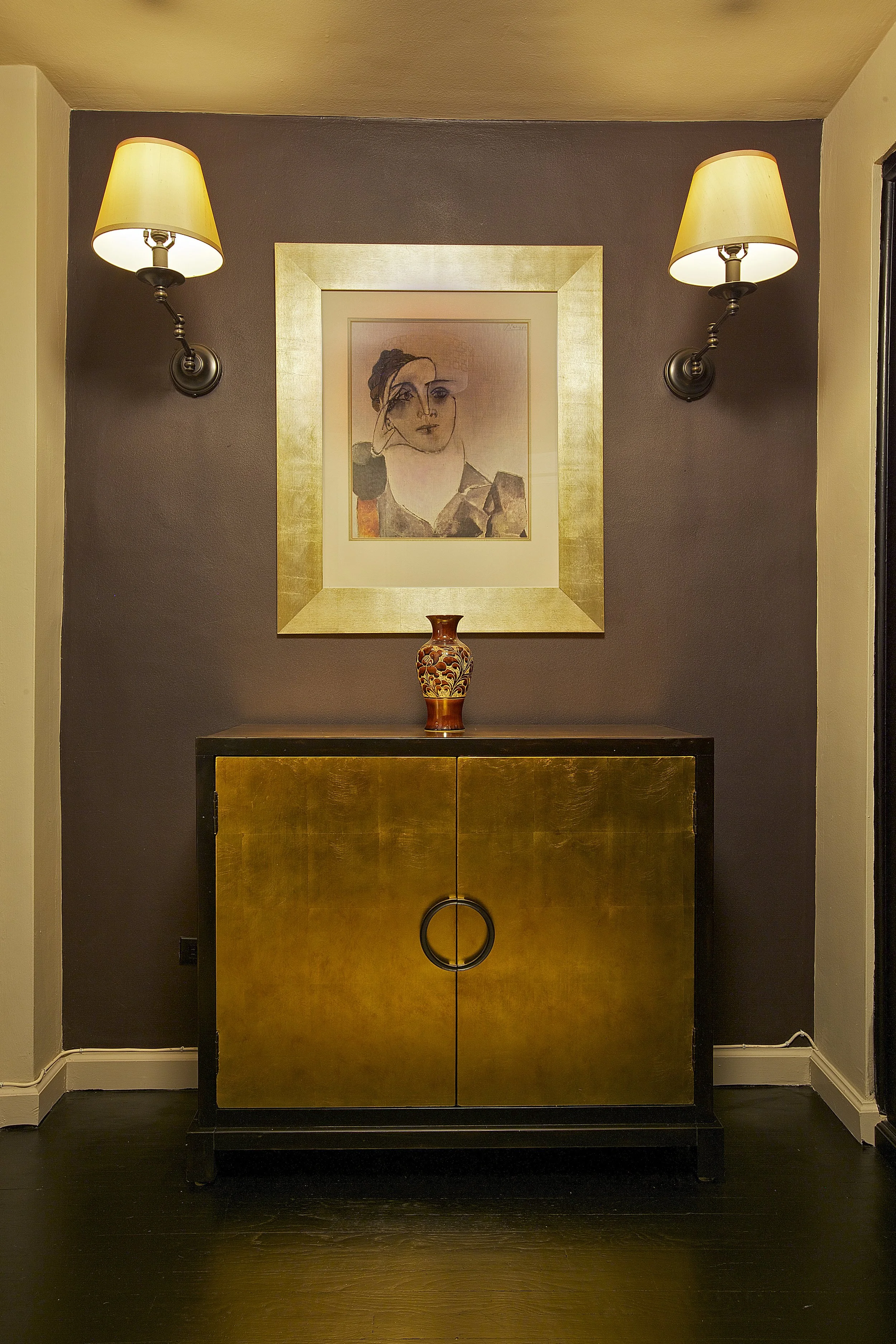 Gold finish Entrance cabinet  and black detail in a foyer, flanked by classic light  sconces