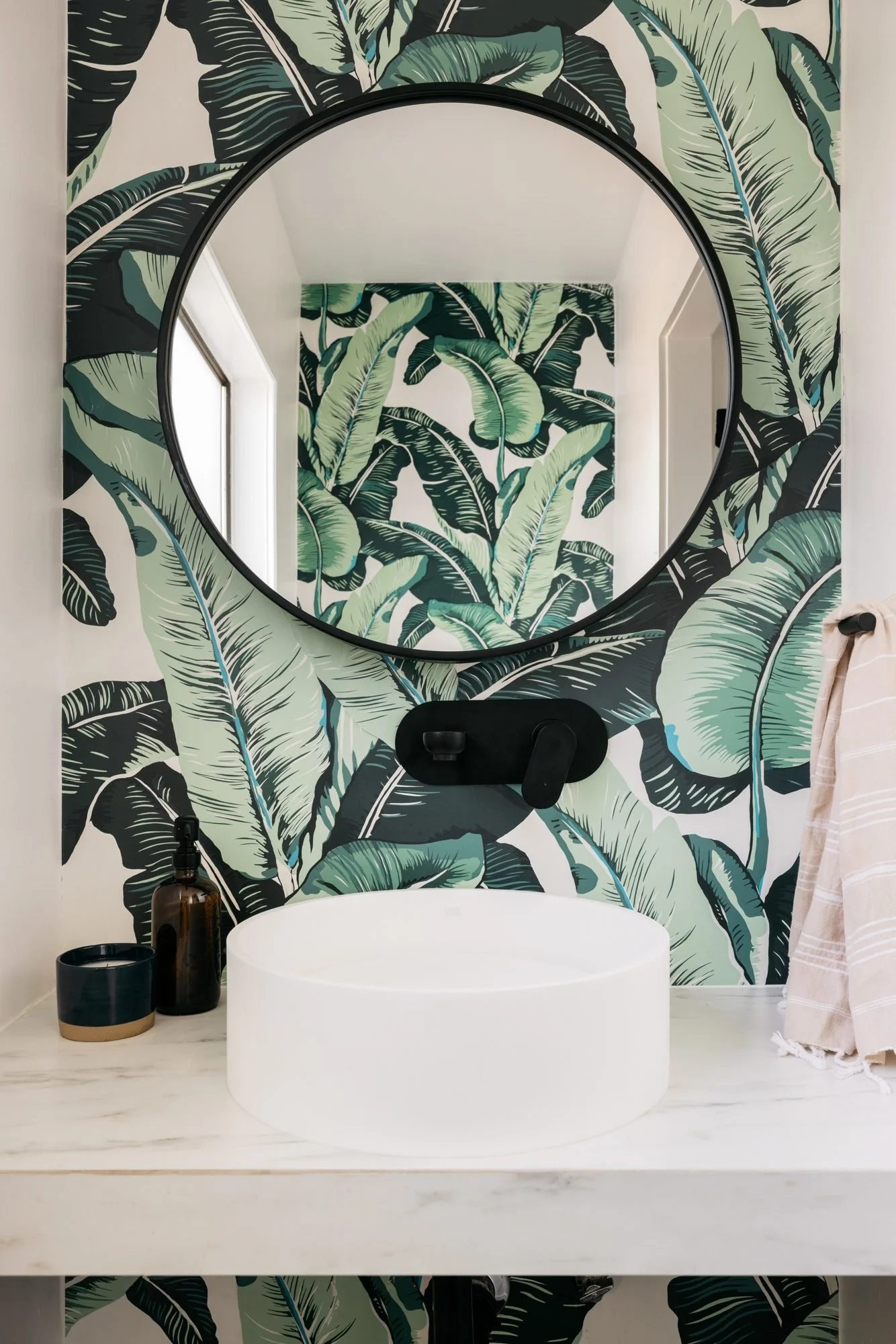 Powder room with green banana-leaf wallpaper, round black mirror and white vessel sink