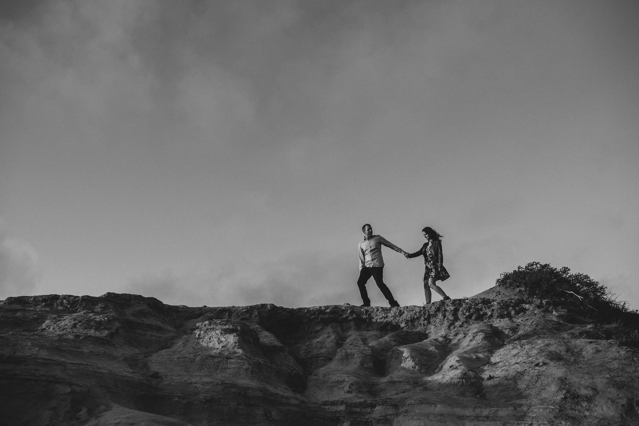 A man leads his fiancé across the jagged ridge line high above the cliffs at Torrey Pines State Reserve.