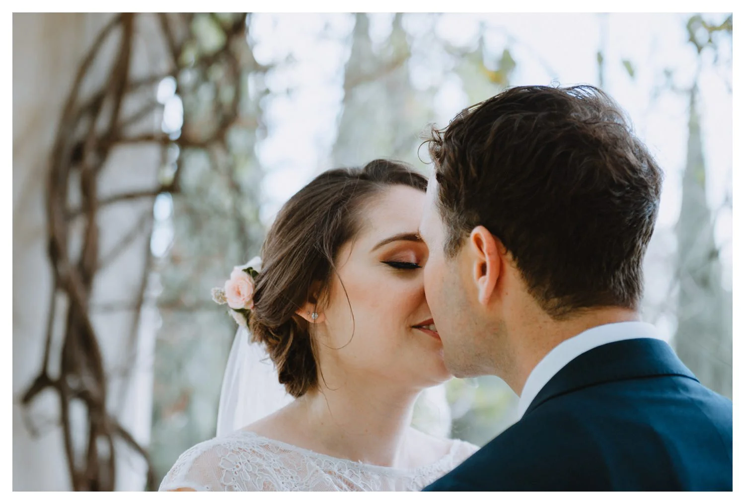 A couple kissing underneath ivy vines on their wedding day