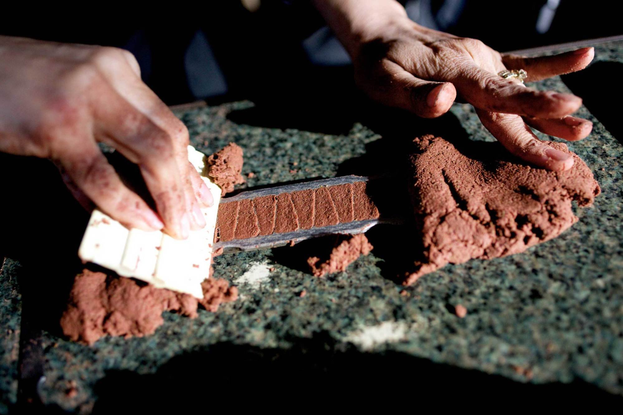 Person sculpting a brick with a hand-shaped tool on a rough stone surface.