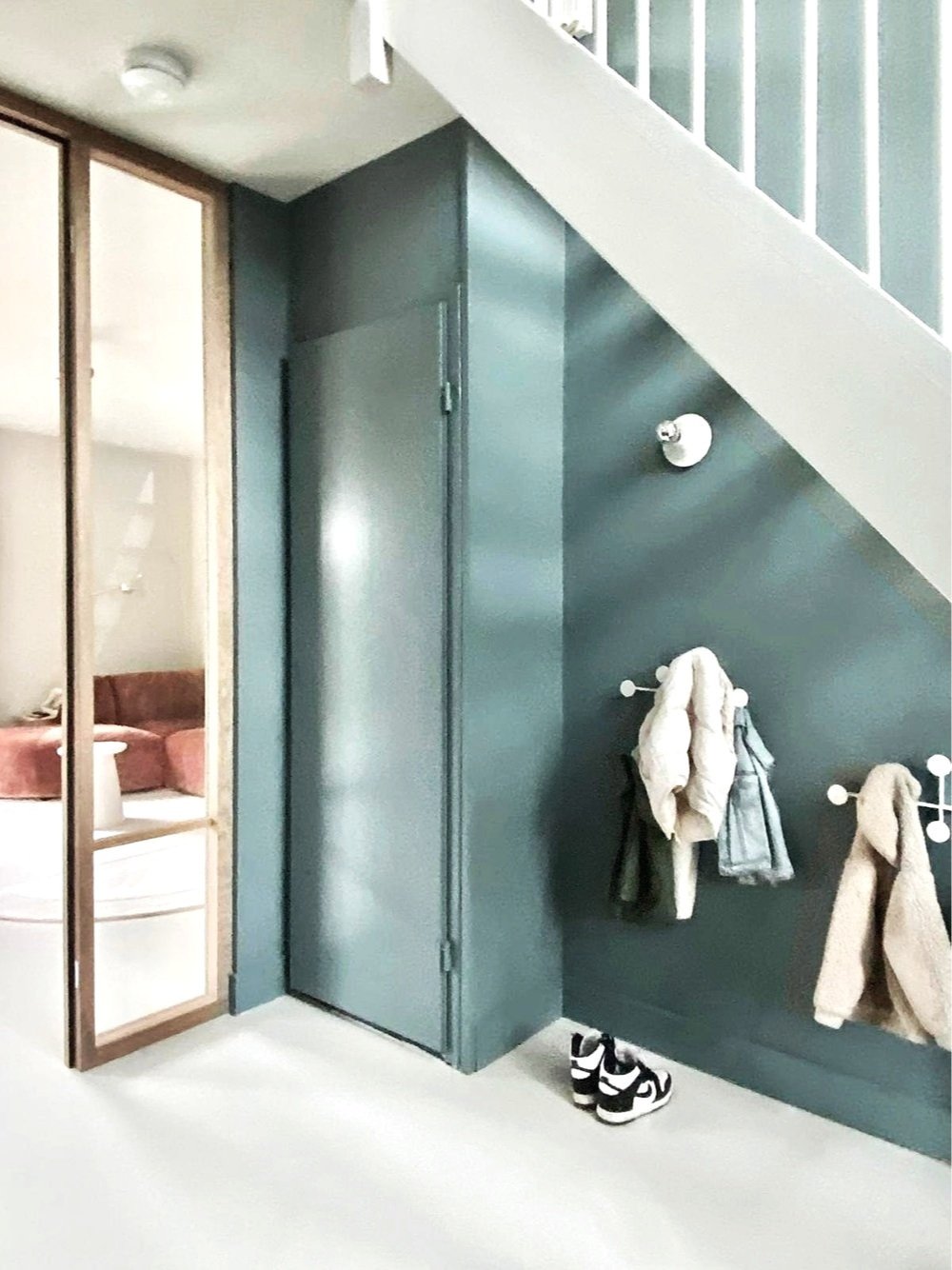 Inrichting van een entreehal met een blauwe muur, de nimes van farrow and ball, een open garderobe met kinderjassen en schoenen, onder de trap. glazen deuren in rank eikenhouten frame. verlichting artemide.