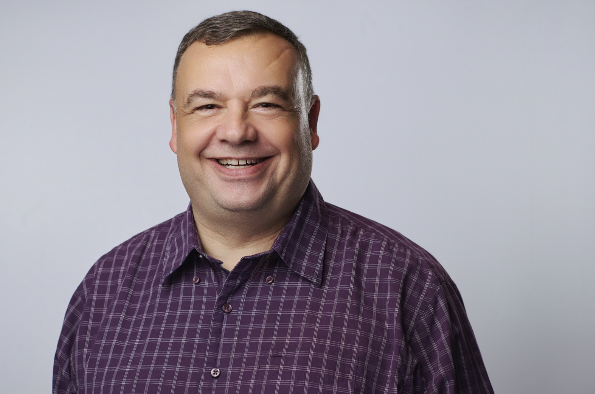 middle aged man in purple striped shirt against a grey backdrop