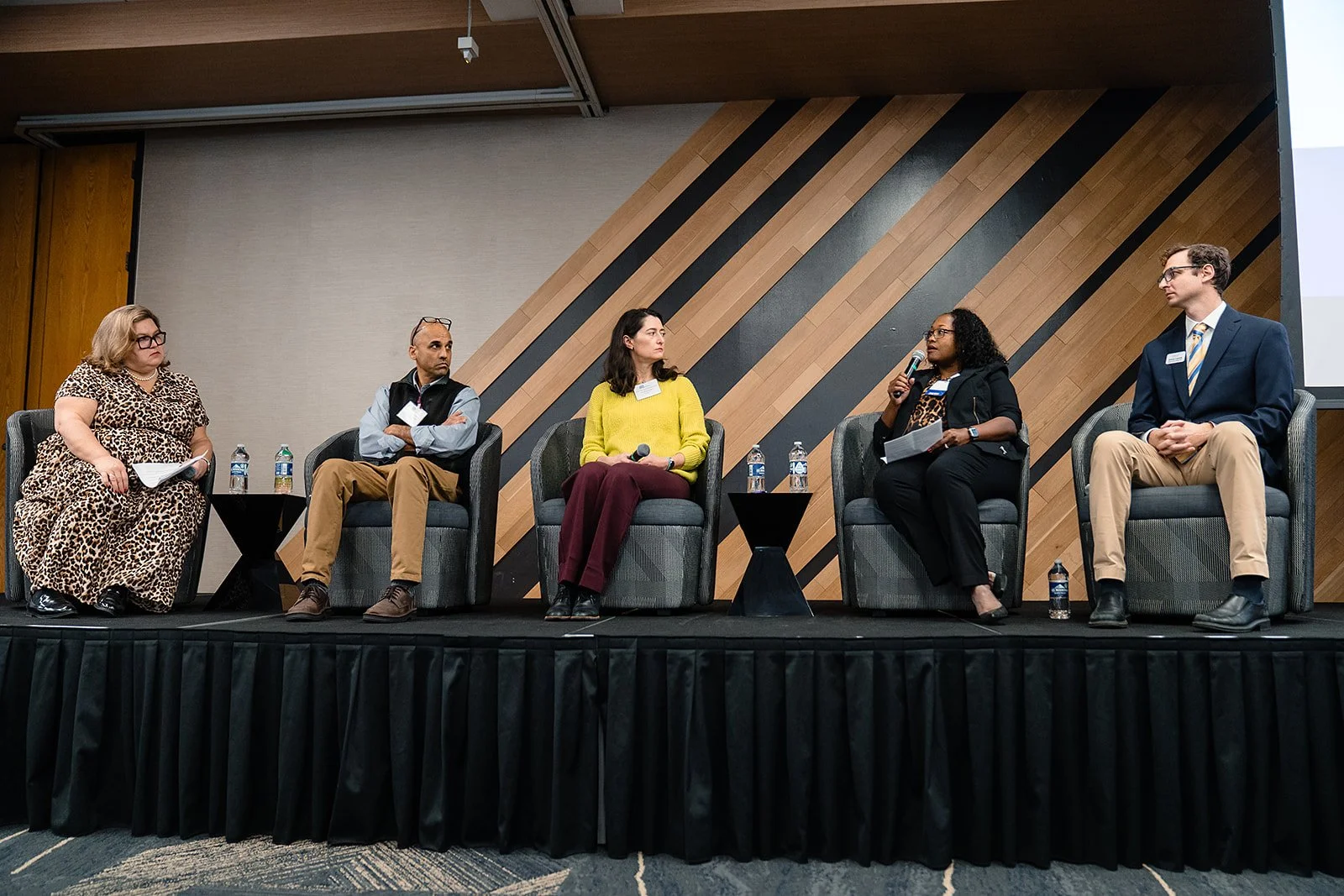 Image is of five panel speakers sitting on stage presenting to an audience out of view.