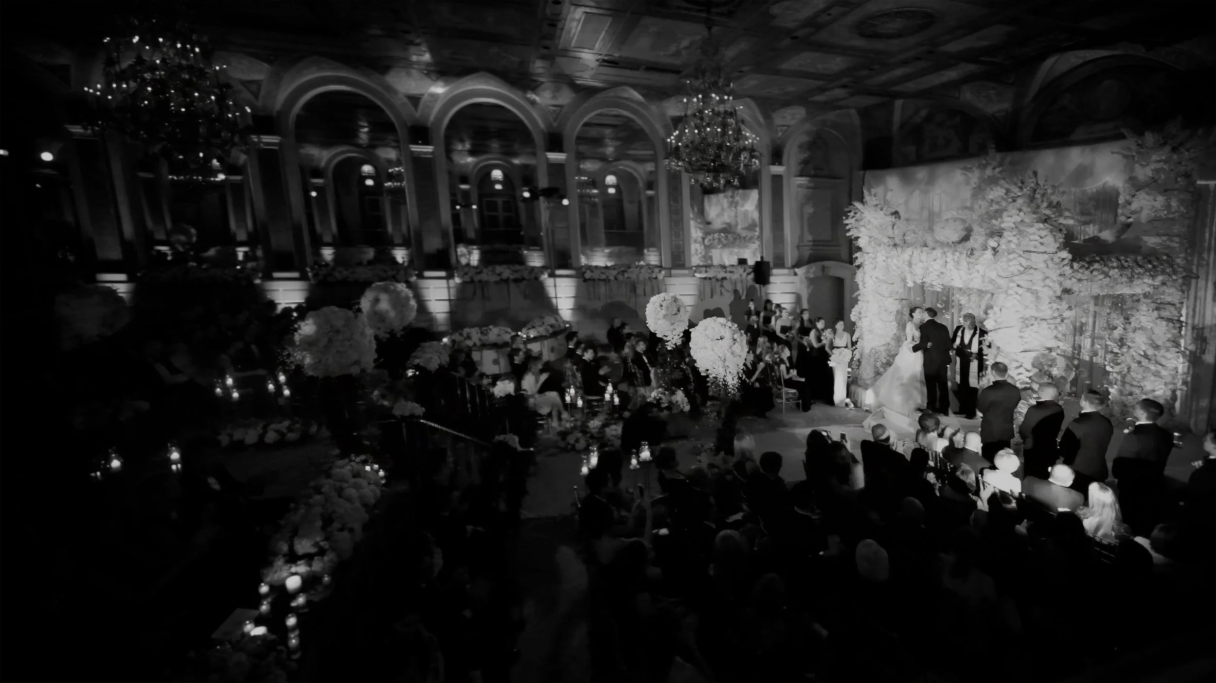Black and white wide view of an elaborate wedding ceremony inside The Plaza Hotel in New York.