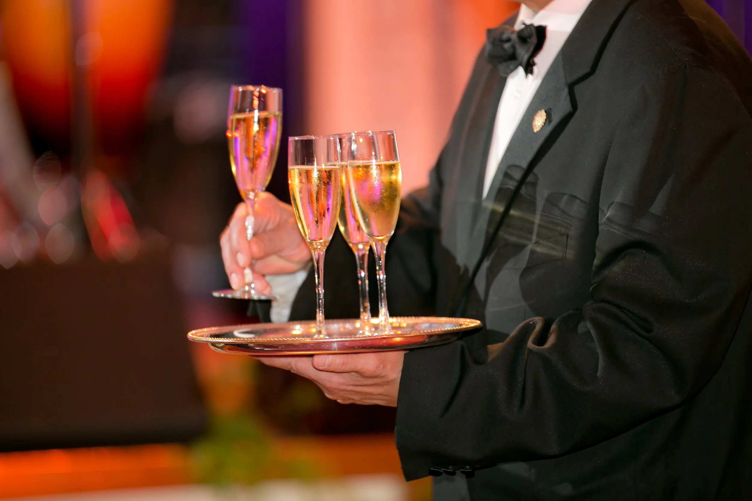 Formal server carrying a silver tray of champagne flutes during an elegant wedding reception at The Plaza Hotel.