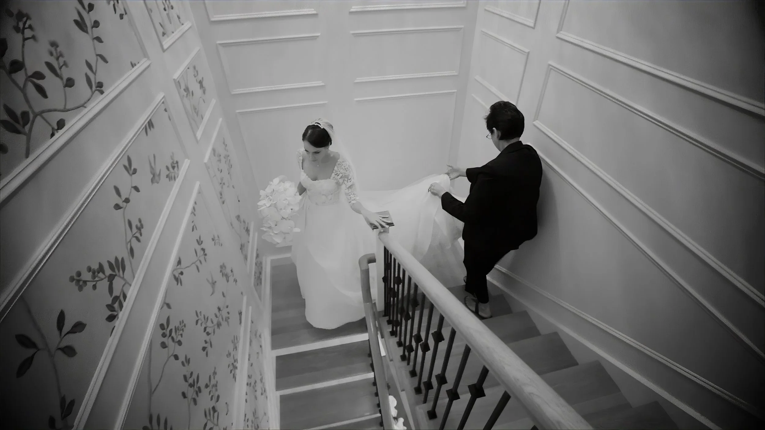 Bride walking up a staircase at The Plaza Hotel as an attendant carries her gown.