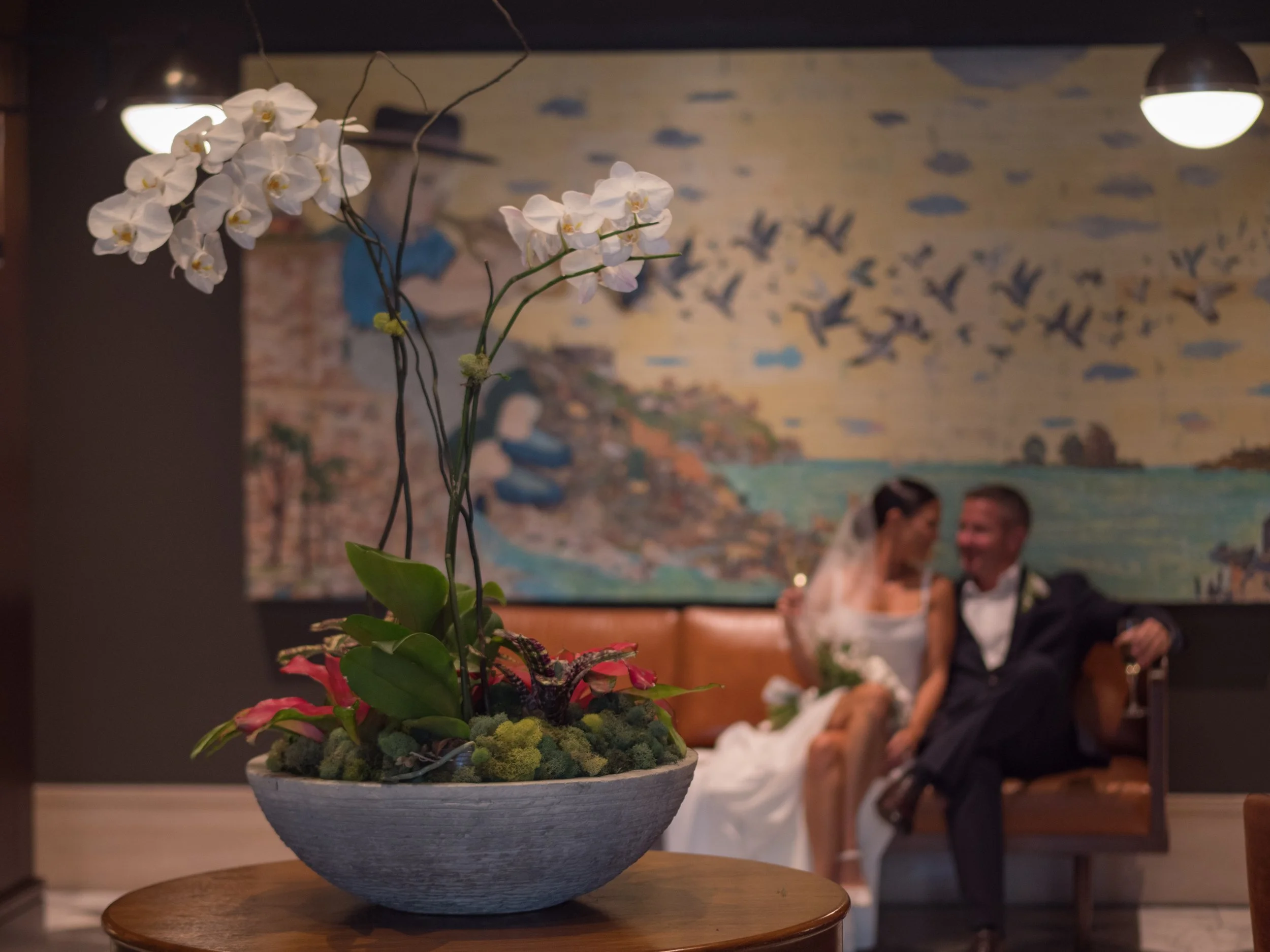 Kate and Ryan seated together in a Perry Lane Hotel lounge, photographed through foreground orchids