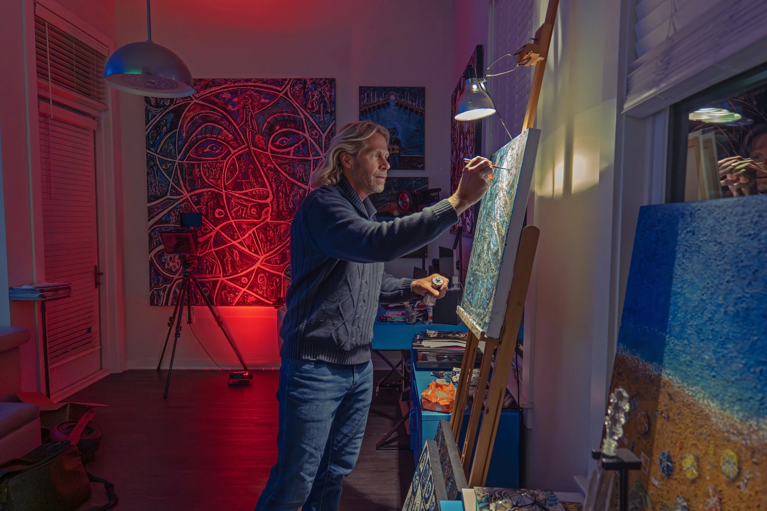 Artist Charles Maring painting at an easel in his Savannah art loft with The Inside Out illuminated behind him.