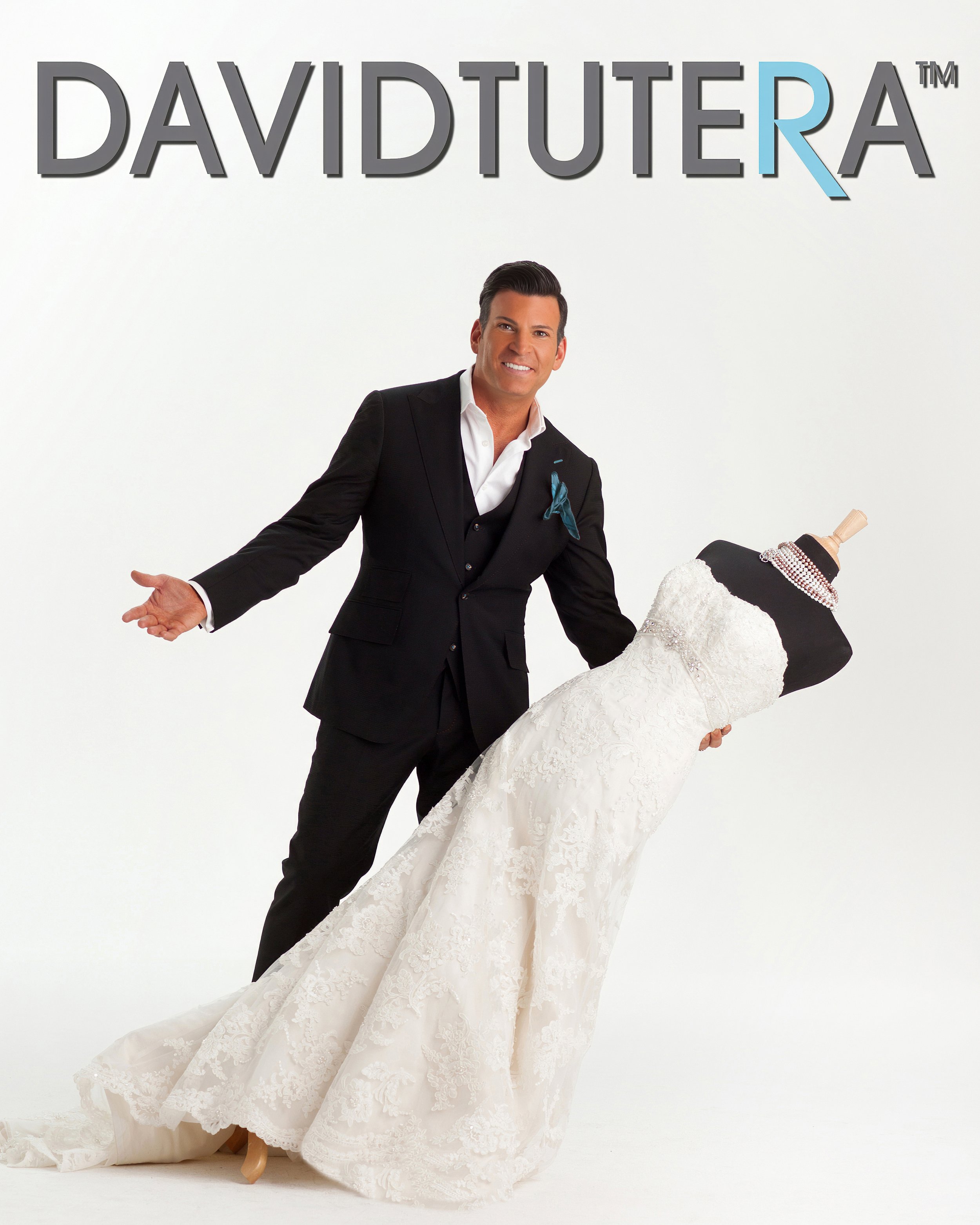 David Tutera presenting a white bridal gown in a promotional brand portrait photographed by Charles Maring.