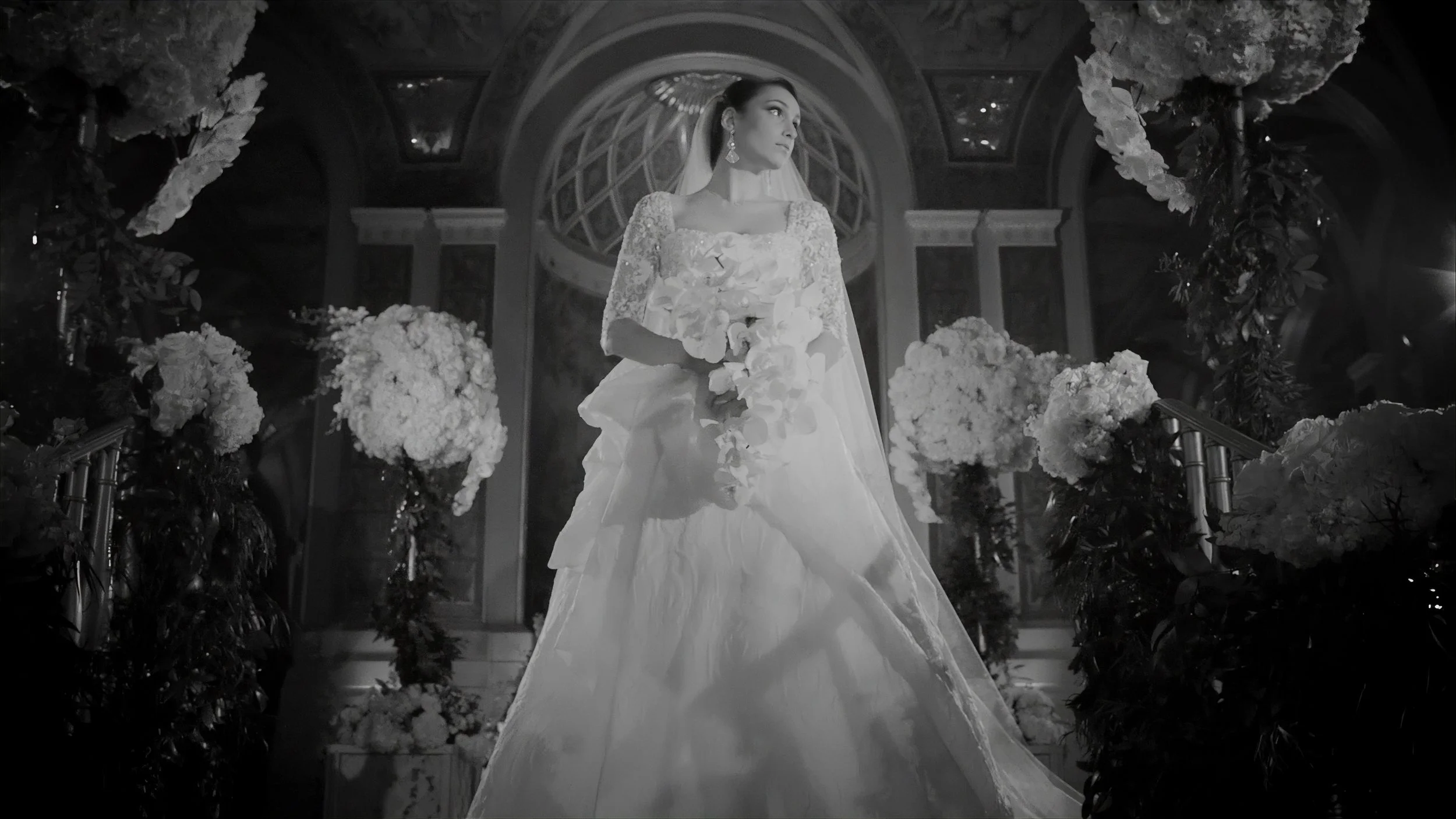 Bride holding orchids beneath the ornate architecture of The Plaza Hotel in a black and white wedding portrait.