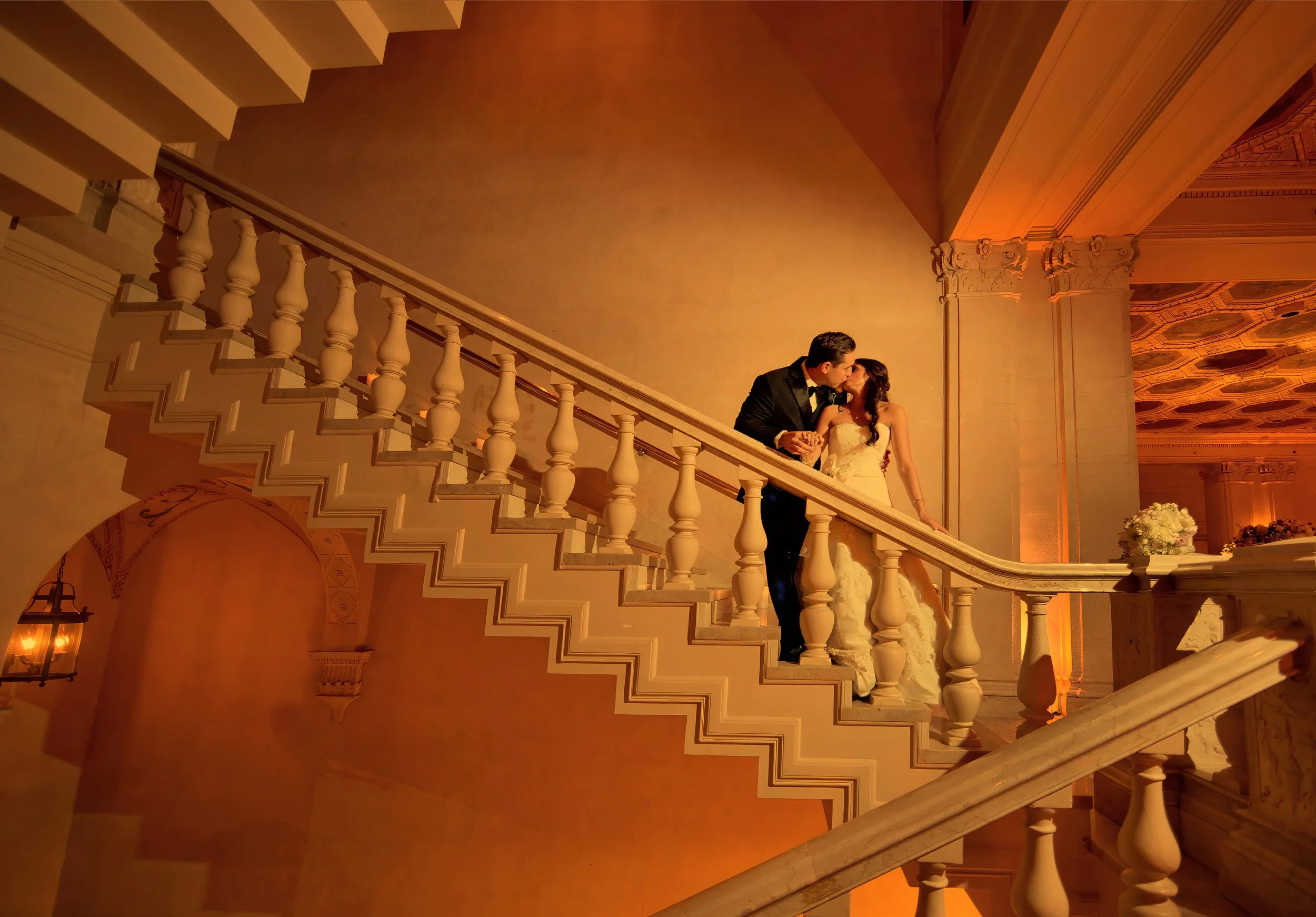 Bride and groom kiss on an ornate staircase illuminated by warm amber light during their New York City wedding.