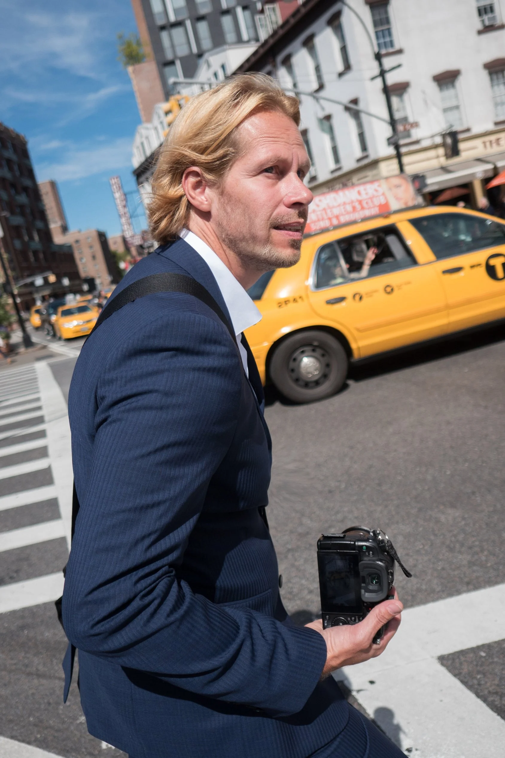 Charles Maring walks through Manhattan carrying a camera as yellow taxis move along the city streets.