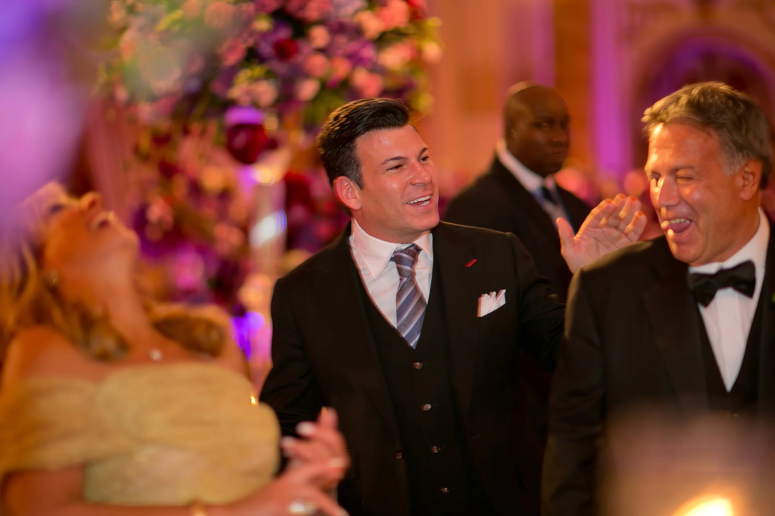 Event designer David Tutera laughing with family members during a lively wedding reception at The Plaza Hotel in New York City.