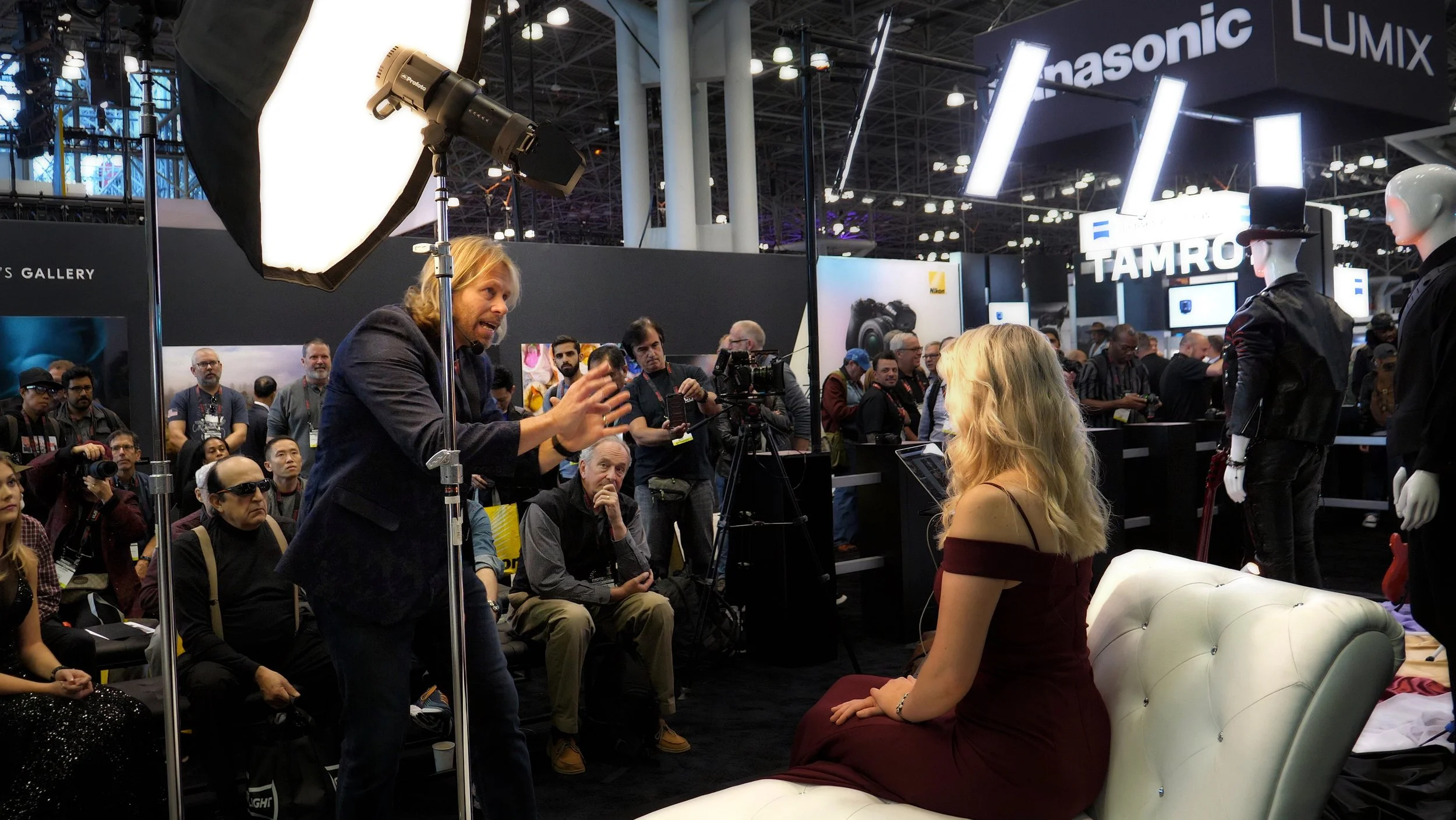 Charles Maring demonstrates live lighting and posing techniques for a large audience inside a conference booth at the Javits Center in New York City.