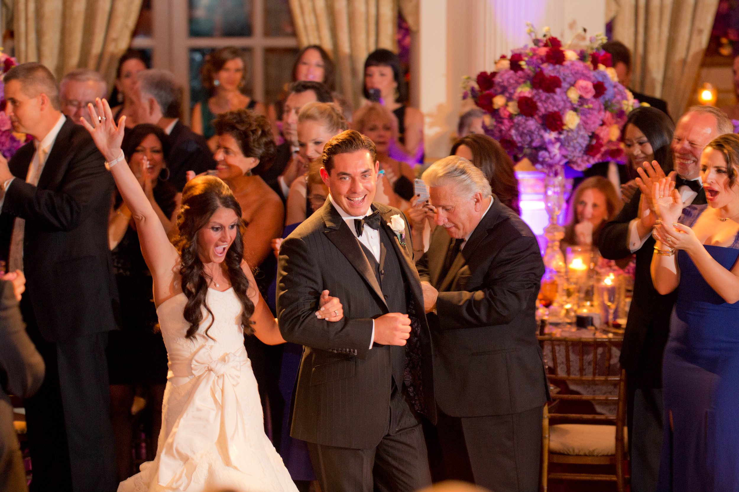 Bride and groom make their grande entrance and celebrate with family and guests during a lively wedding reception filled with colorful floral arrangements at The Plaza Hotel.