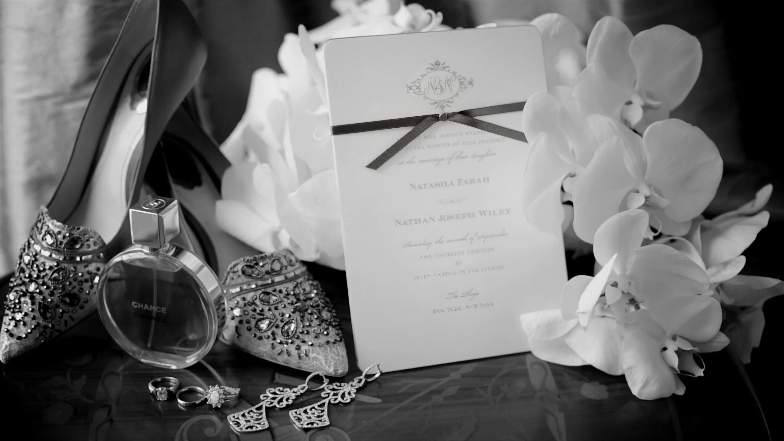 Bridal shoes, Chanel perfume, wedding rings, orchids and invitation photographed in black and white at The Plaza Hotel.