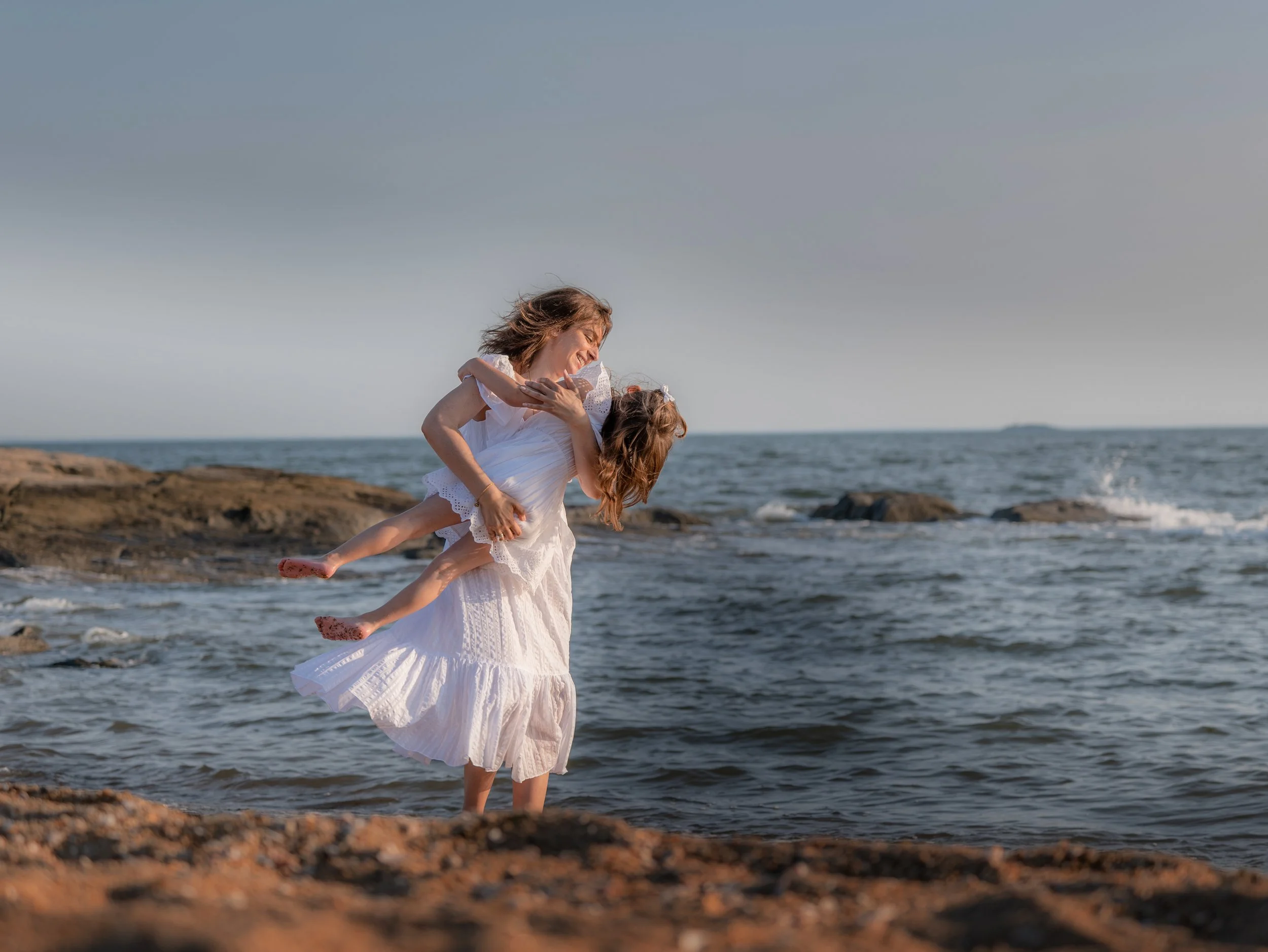A spontaneous moment between a mother and daughter beside the ocean, photographed between the poses.