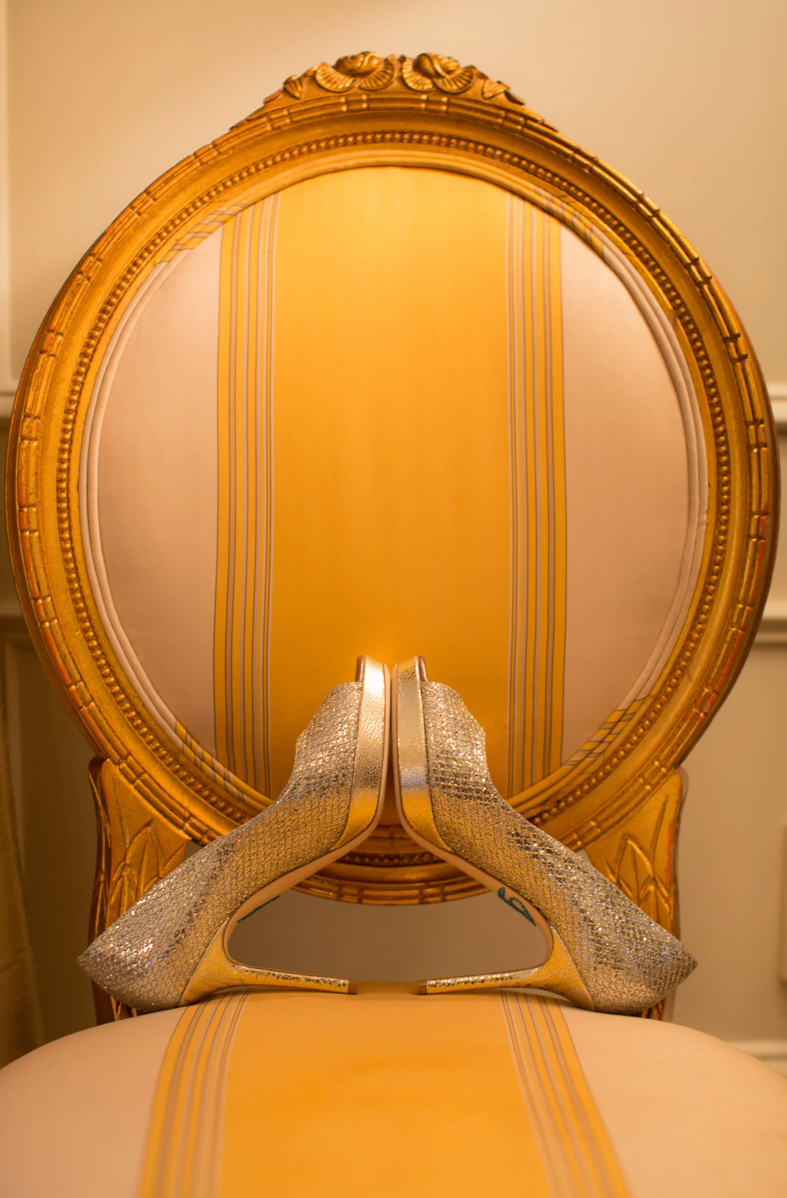 Sparkling silver bridal shoes arranged symmetrically on a gold-framed upholstered chair inside The Plaza Hotel.
