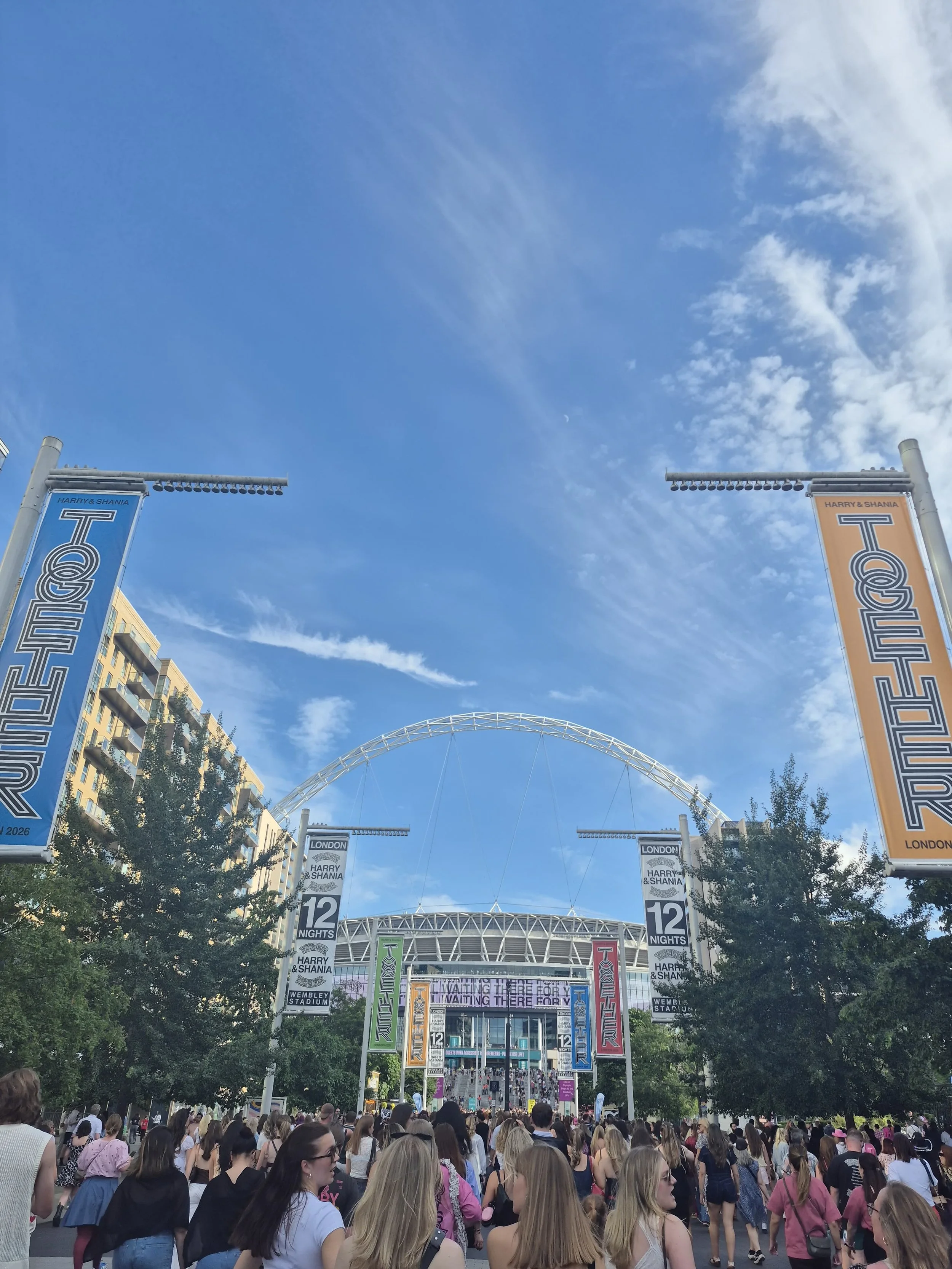 Crowds walking towards Wembley Stadium under Harry Styles Together tour banners before the Saturday 20 June 2026 show.