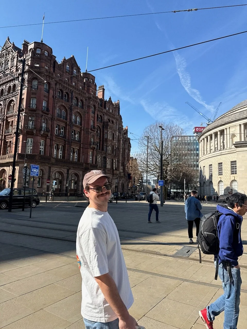 Greg Corrigan looking back and smiling while walking through central Manchester on a sunny day.