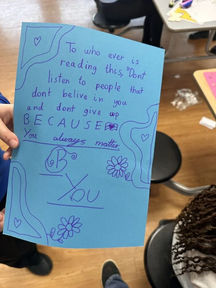 A handwritten letter on blue paper with hearts and flowers drawn around it