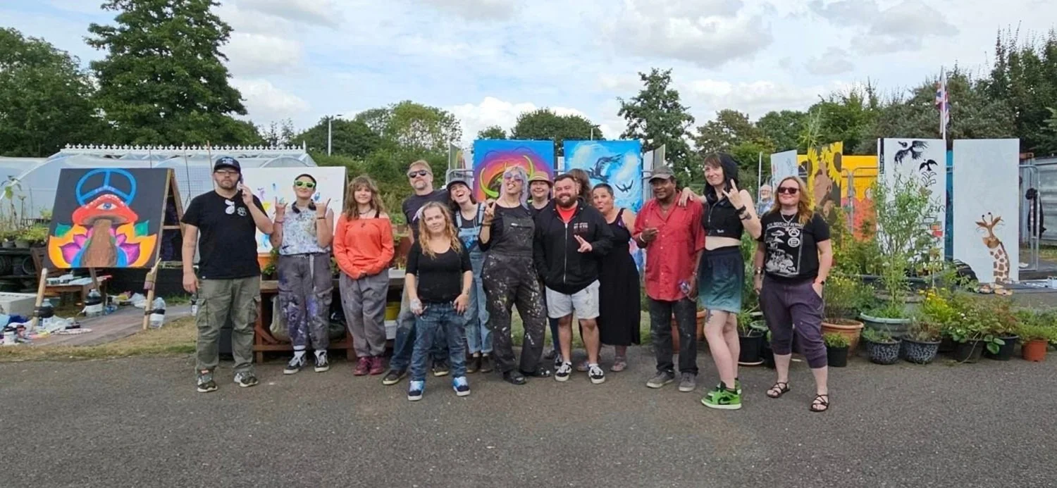 A group of artists standing together in front of big colourful paintings at an Angry Pencil paint jam