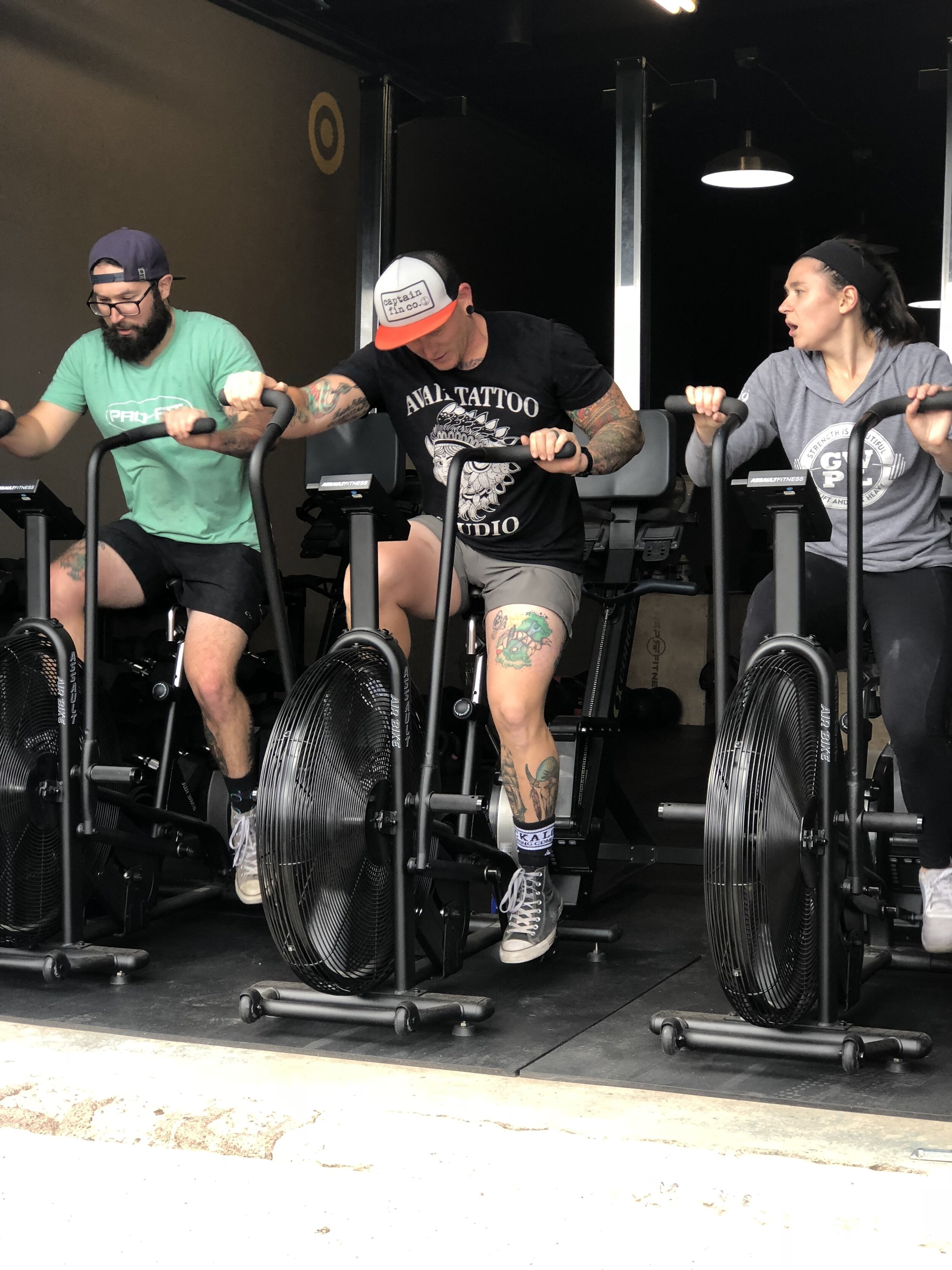 three people riding assault bikes at a gym