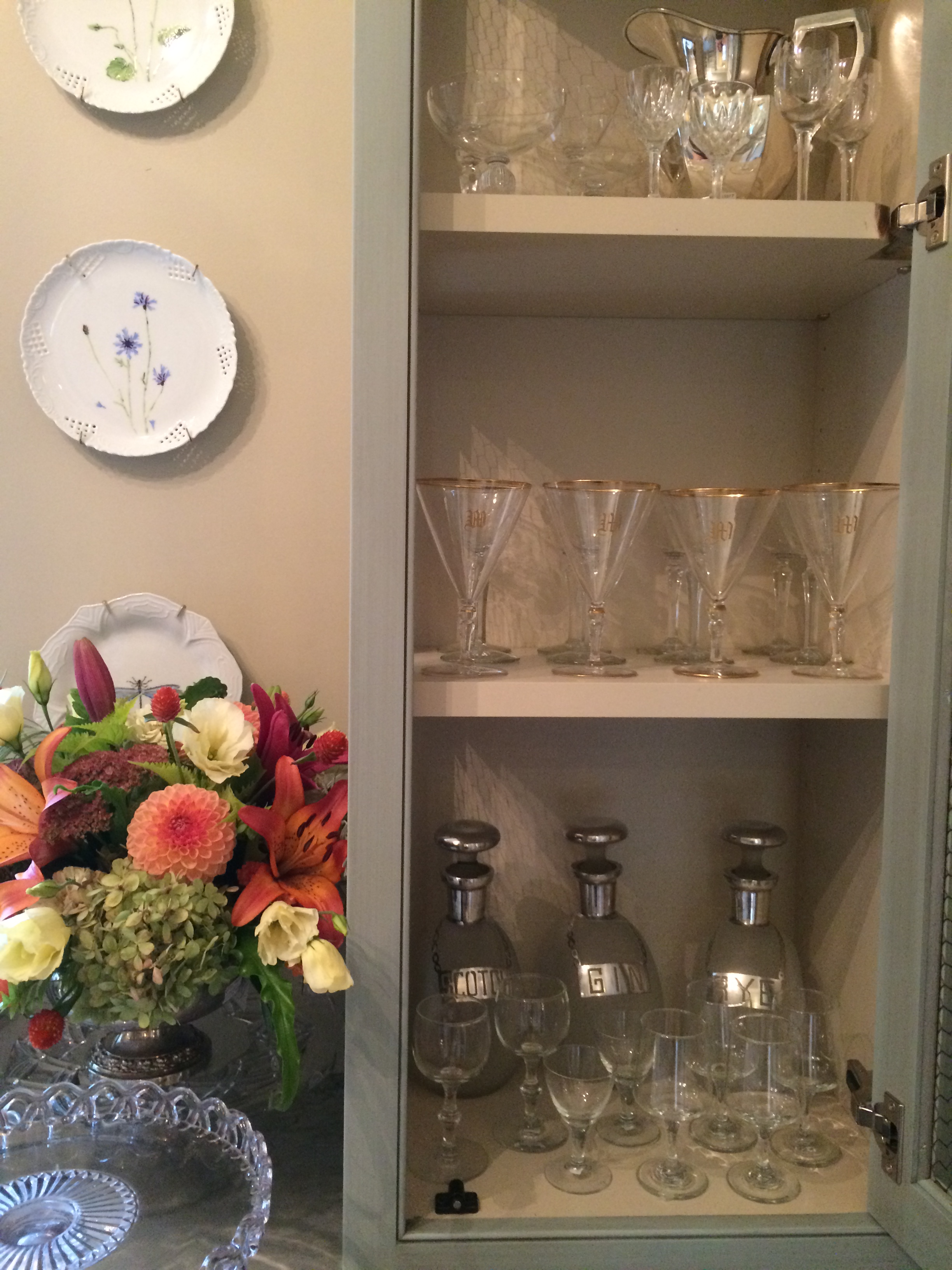 Stem and bar ware in cabinets and flowers in a vintage silver plate flower arrangers.