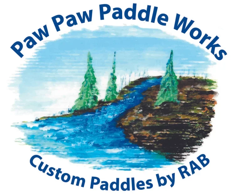 A logo with a painted scene of a river flowing through rocky terrain with evergreen trees on either side, and the text "Paw Paw Paddle Works" at the top and "Custom Paddles by RAB" at the bottom.
