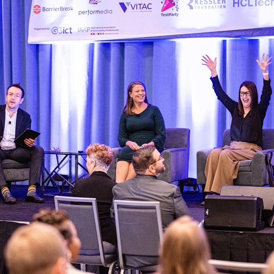 Caitlin is seated cross-legged on a stage at the m-Enabling conference with other panelists. She is laughing, wears a green dress with her medium length brown hair down and is visibly pregnant.