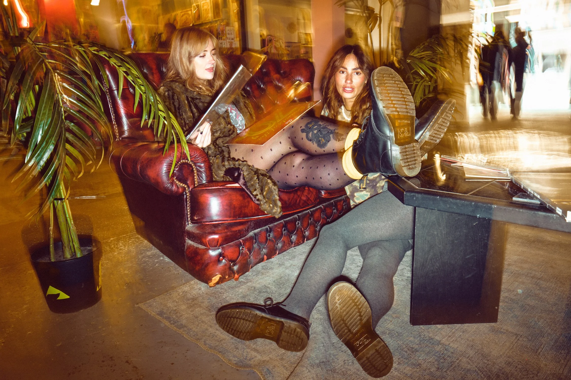 Two models wearing Dr. Martens boots browsing vinyl records during a documentary-style fashion campaign shoot.