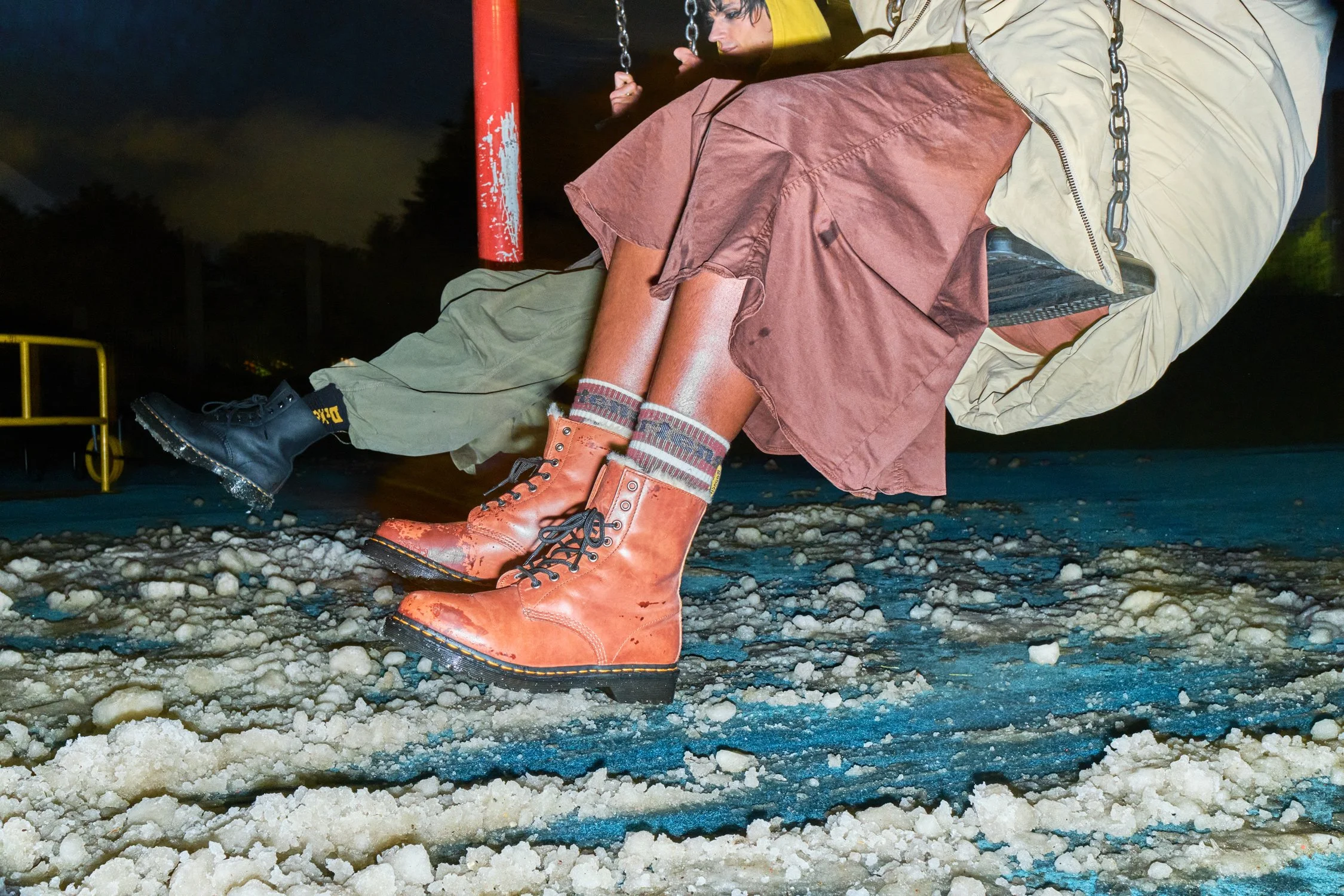Models playing on swings in snow during the Dr. Martens Reclaim Winter campaign in Manchester.