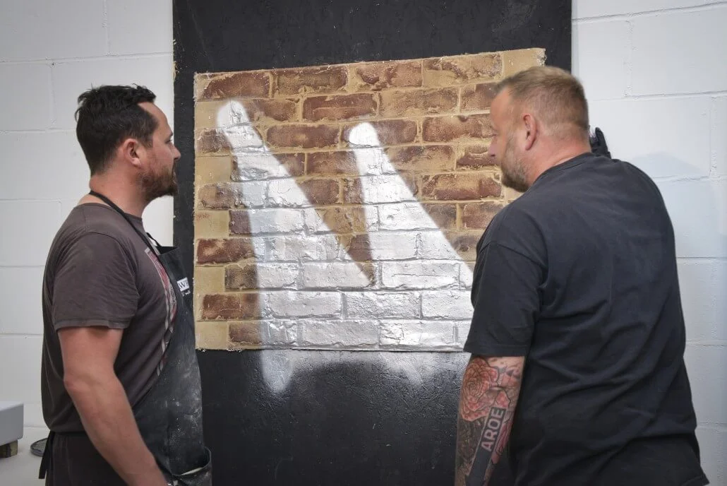 Ian Zawadzki and Aroe discussing artwork on one of our fauxbrick walls.
