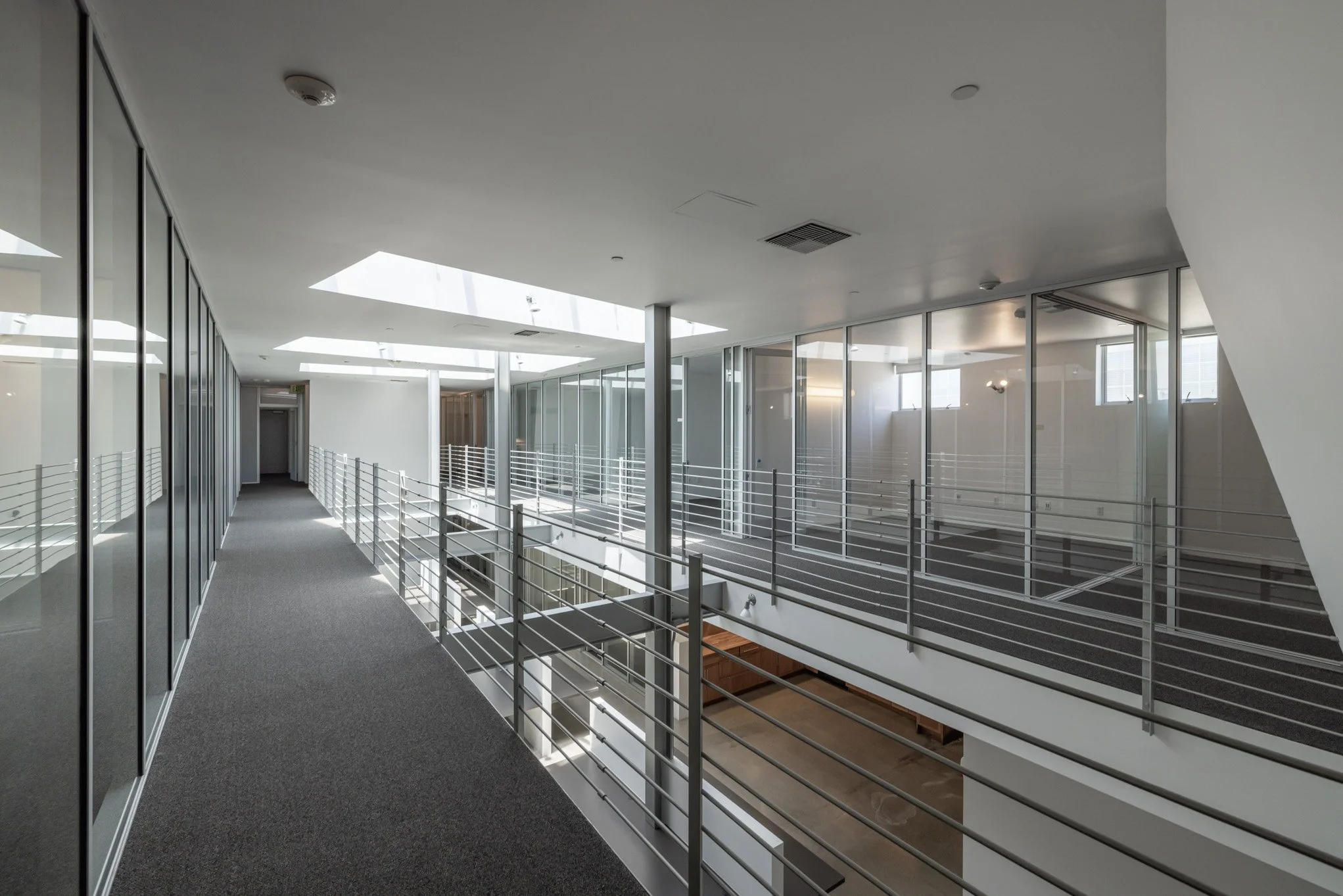 Empty modern office corridor with glass walls, metal railings, and skylights.