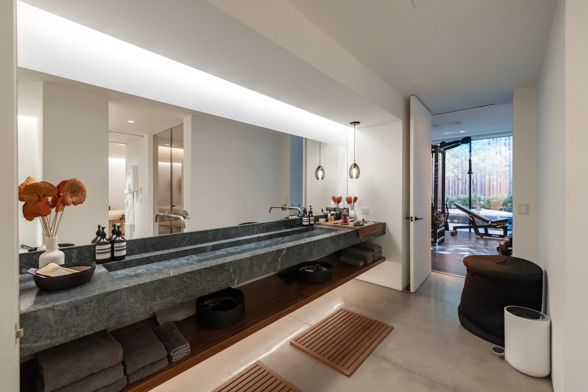 Modern bathroom with a marble countertop, two sinks, and a window overlooking a garden with outdoor gym equipment.