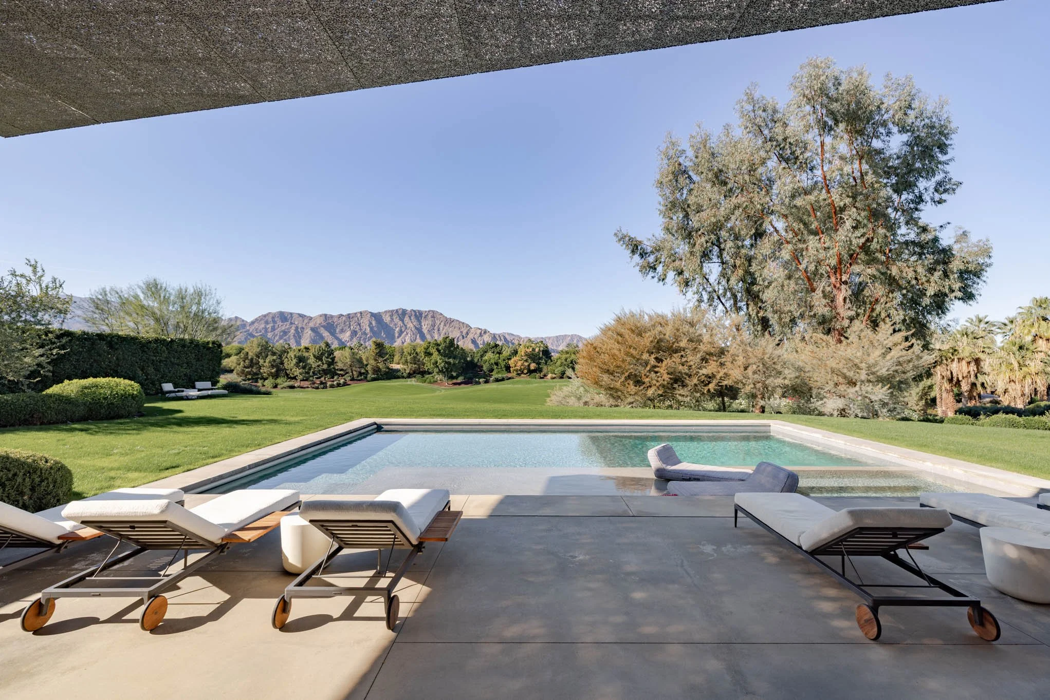 Luxury backyard with a modern swimming pool, lounge chairs, lush green lawn, trees, and mountains in the background.