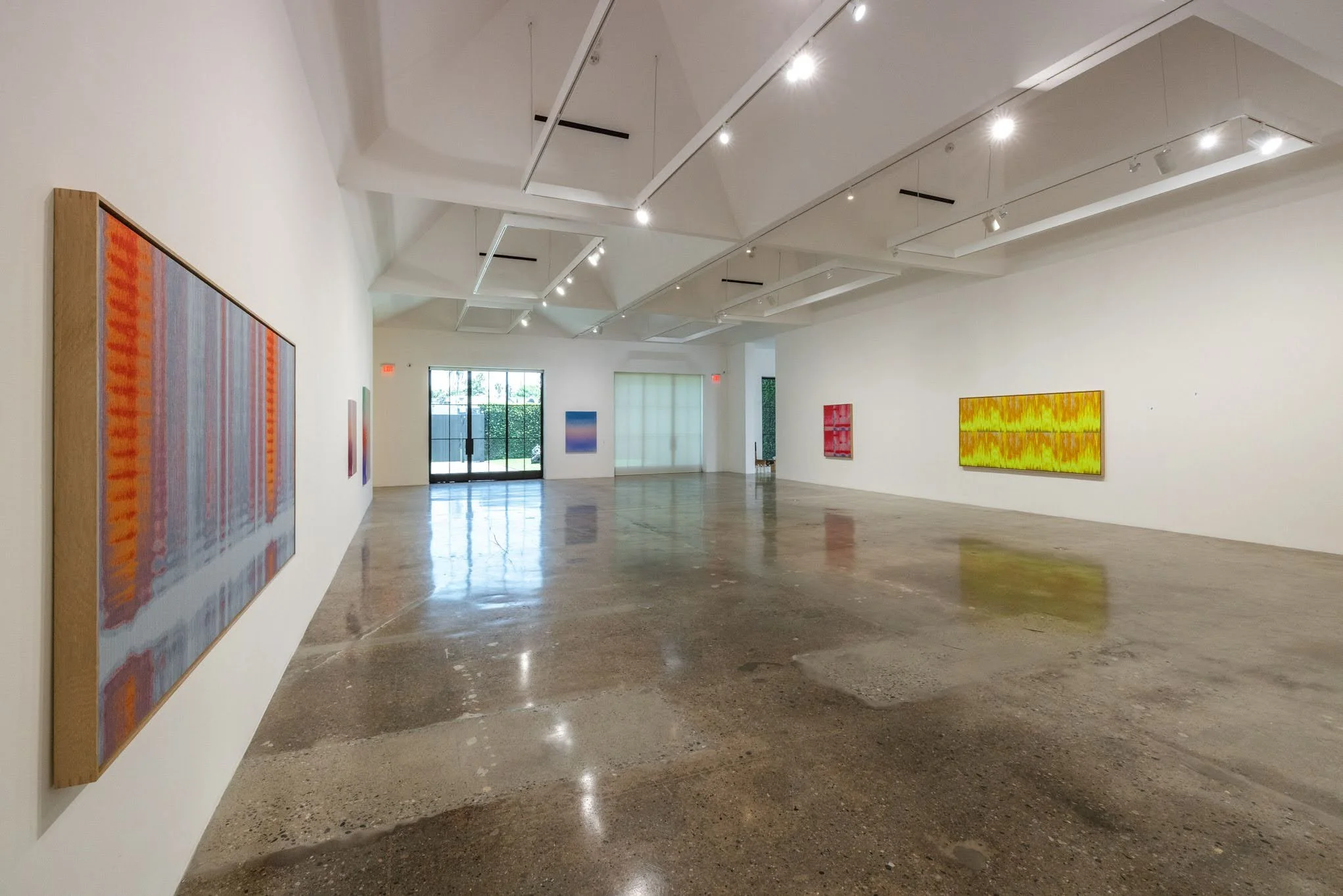 Empty art gallery with white walls, black ceiling, polished concrete floor, and ceiling-mounted lighting fixtures.