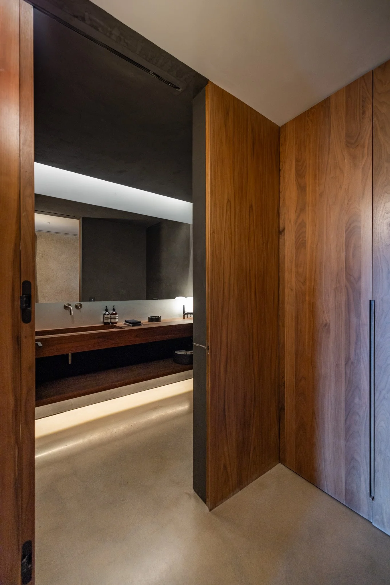 Wooden sliding door opening to a modern bathroom with a wooden vanity and a large mirror.