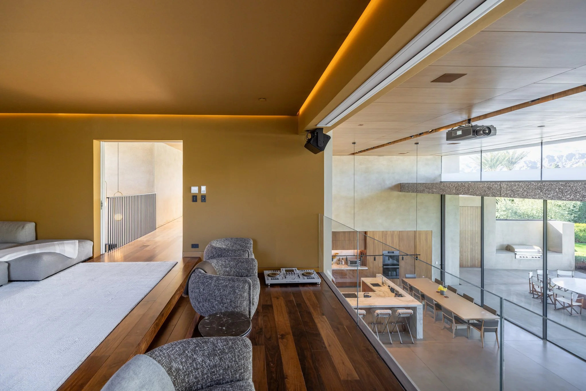 Modern open-concept living and dining area with large floor-to-ceiling windows, hardwood floors, contemporary furniture, and a view of the patio and garden outside.