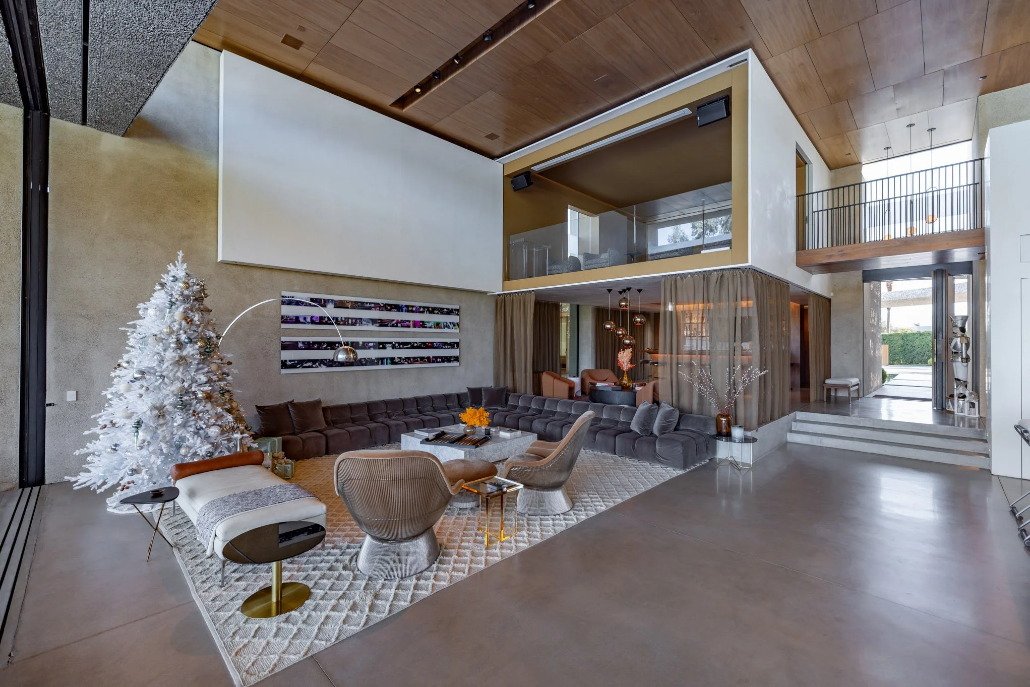 Modern living room with white Christmas tree, sectional sofa, armchairs, and contemporary decor elements.