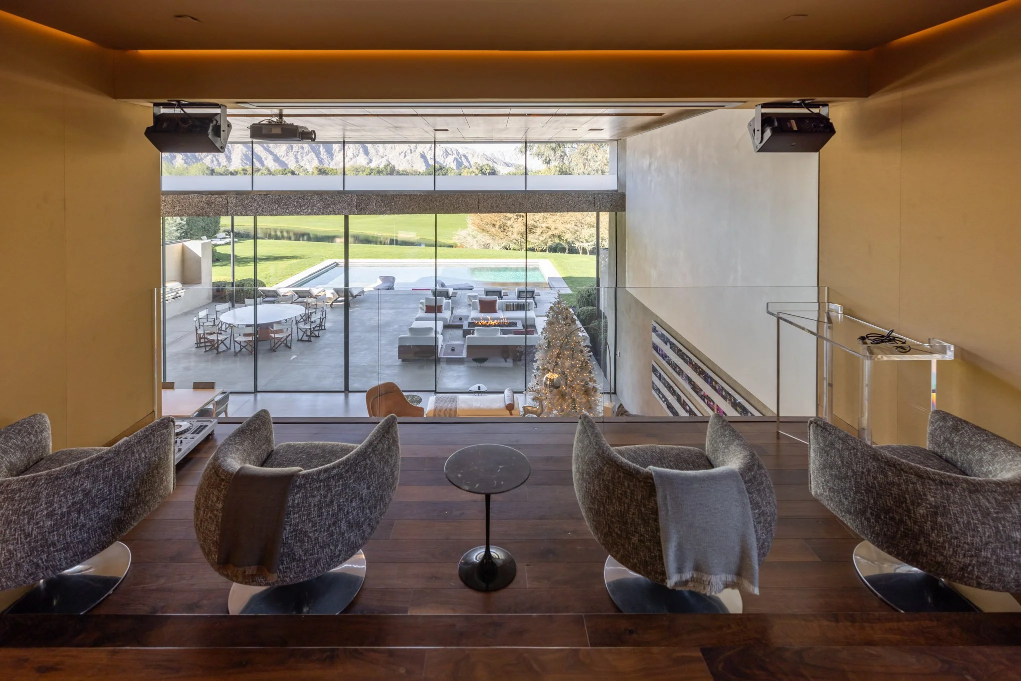 View from an interior house window looking out onto a patio with seating and a pool, with a scenic landscape in the background.