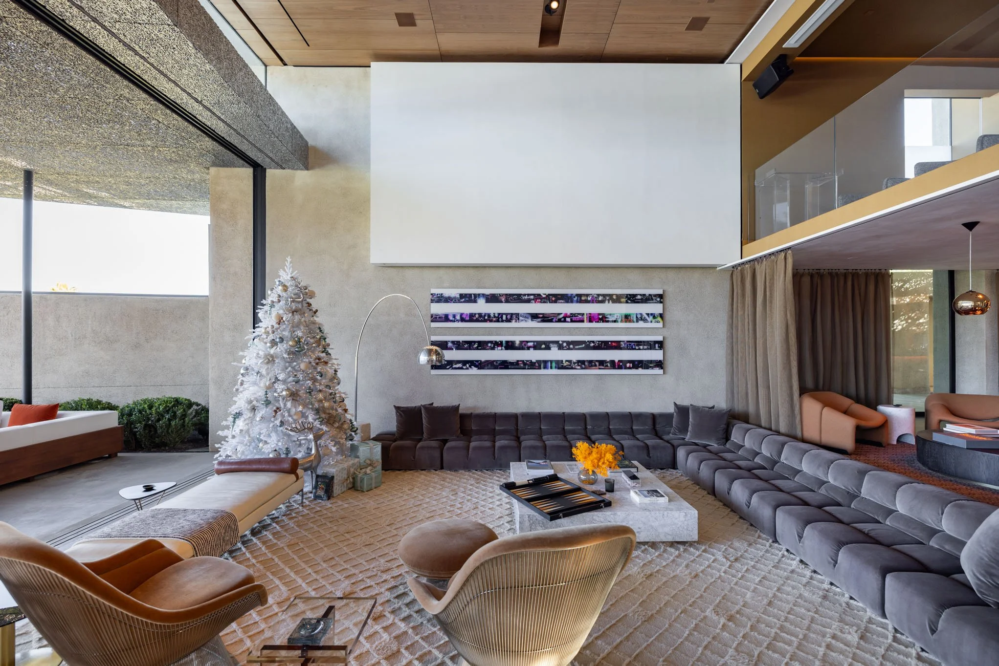 Modern living room with gray sectional sofa, Christmas decorated white tree, abstract art on the wall, and contemporary furniture.