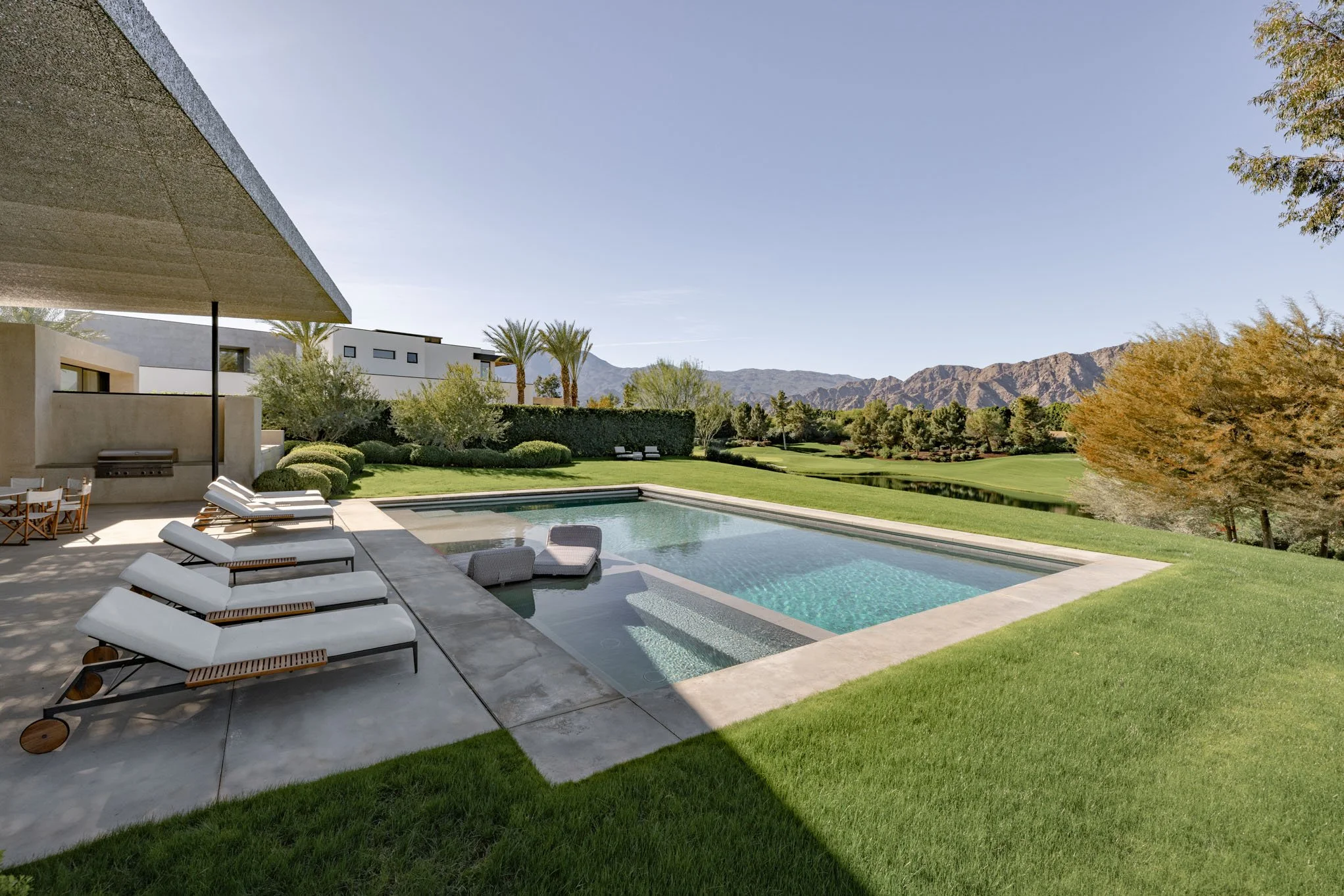 Luxury backyard with a modern swimming pool, surrounded by green grass, trees, and mountain views in the distance.