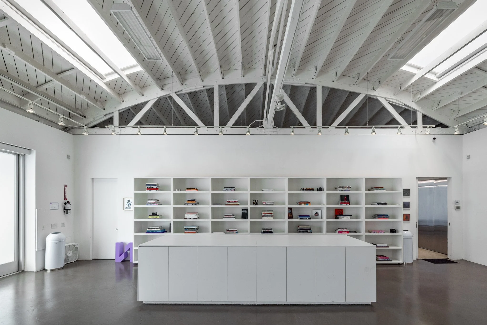 Empty modern library space with white bookshelves, minimalist design, and high vaulted ceiling.